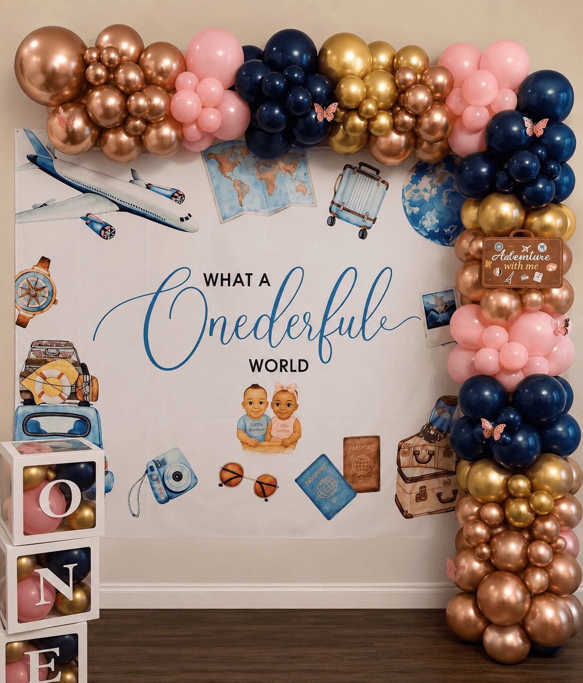 Decorative wall with balloon arch in pink, blue, gold, and rose gold, and travel-themed stickers with the phrase