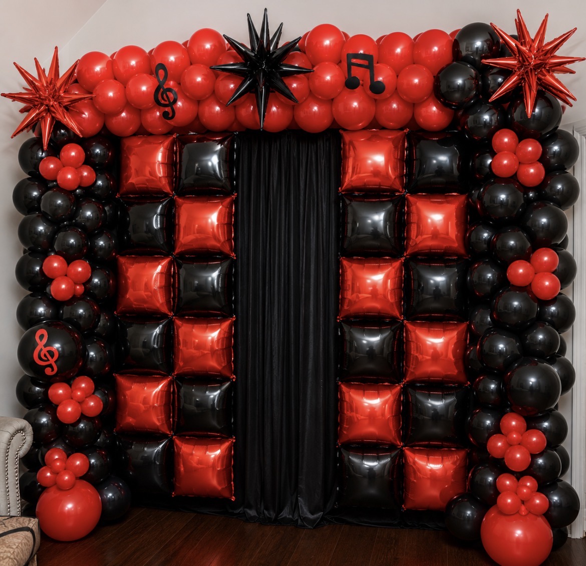 Balloon arch with red and black balloons, musical note and star decorations, and black curtain in the center.