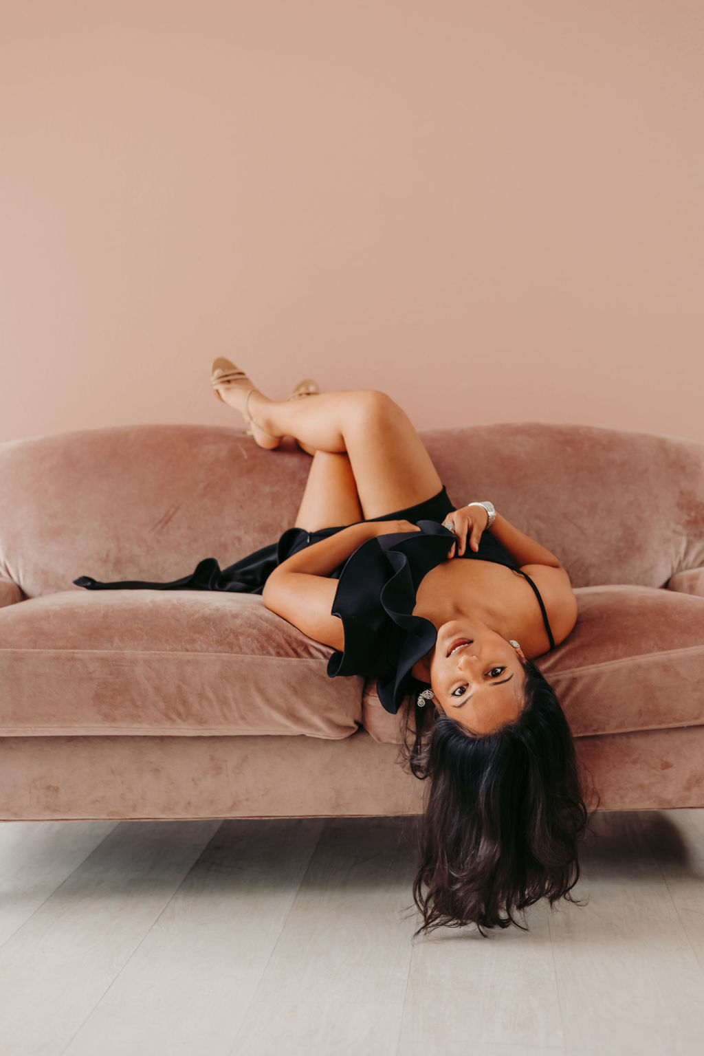 Woman lying upside down on a sofa with legs raised and head hanging off, looking at the camera.