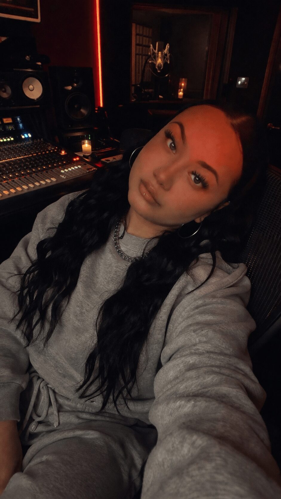 Young woman with long dark hair taking a selfie in a dimly lit recording studio.