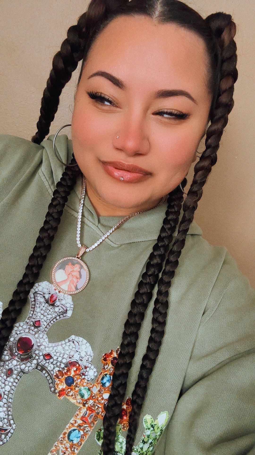 Young woman with braided hair, wearing a green shirt and jewelry, smiling slightly, looking to the side.