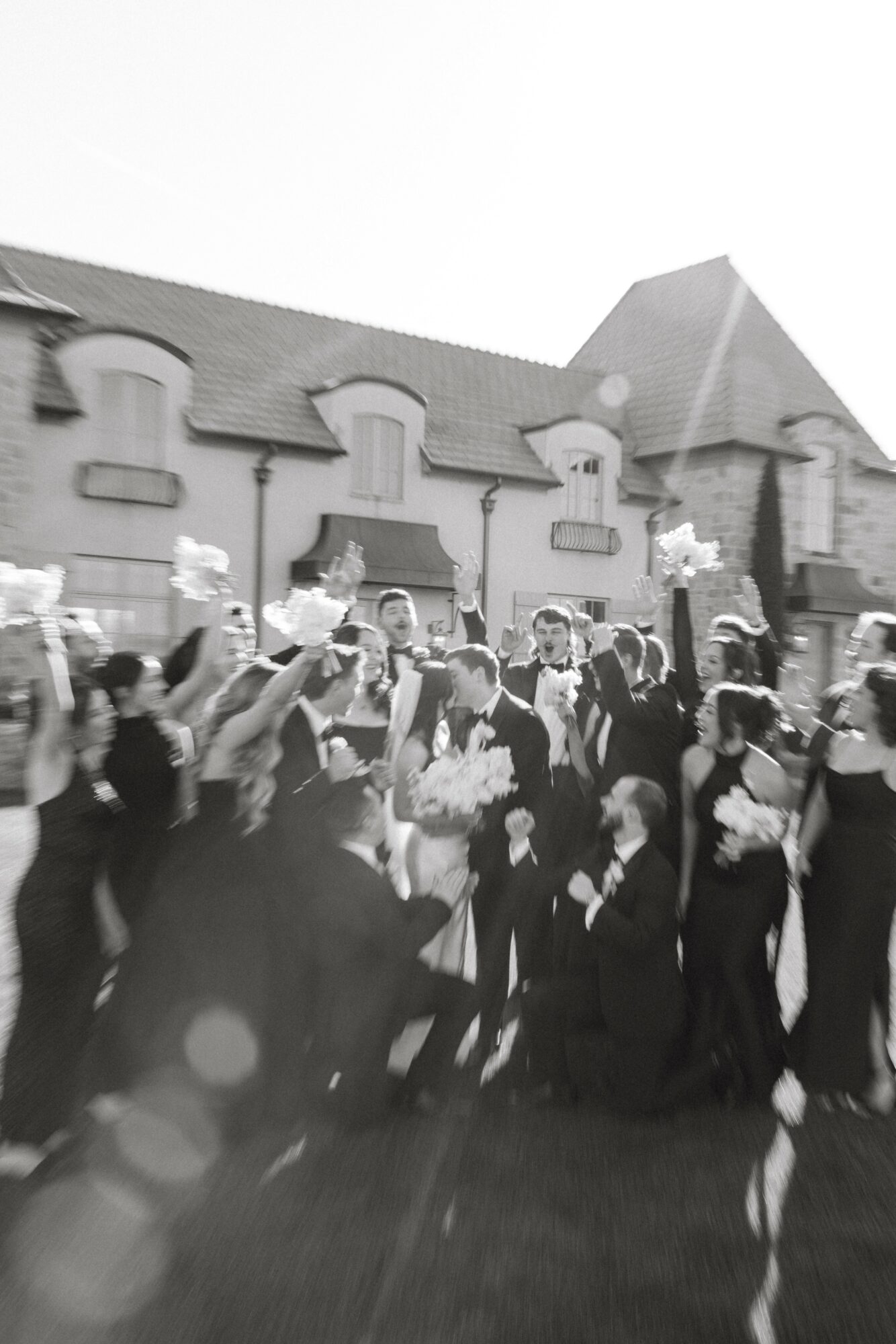 Group of people outdoors in front of a building, some holding flowers, in black and white.