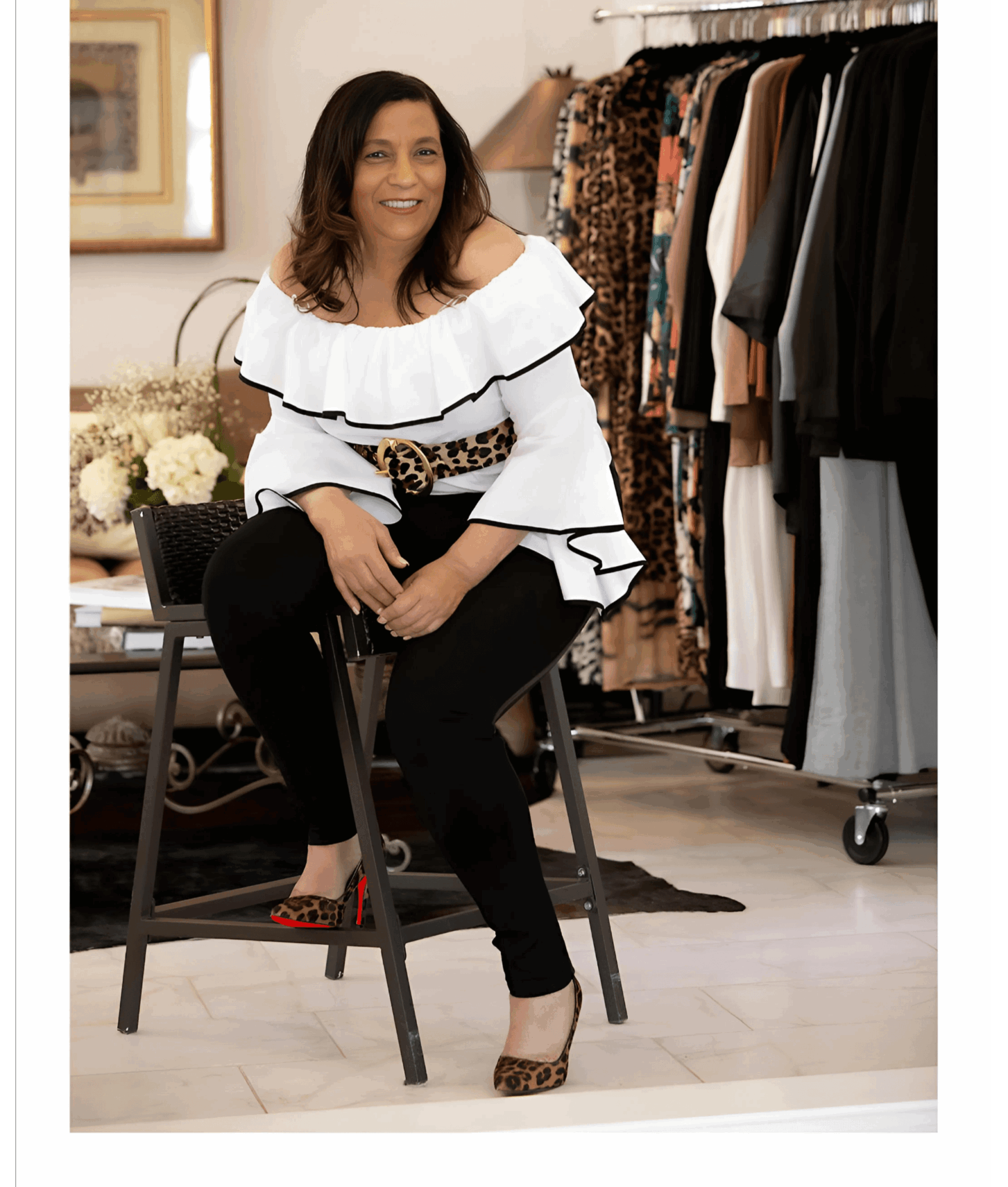Woman sitting on a chair in a clothing store, smiling, with racks of clothes behind her.