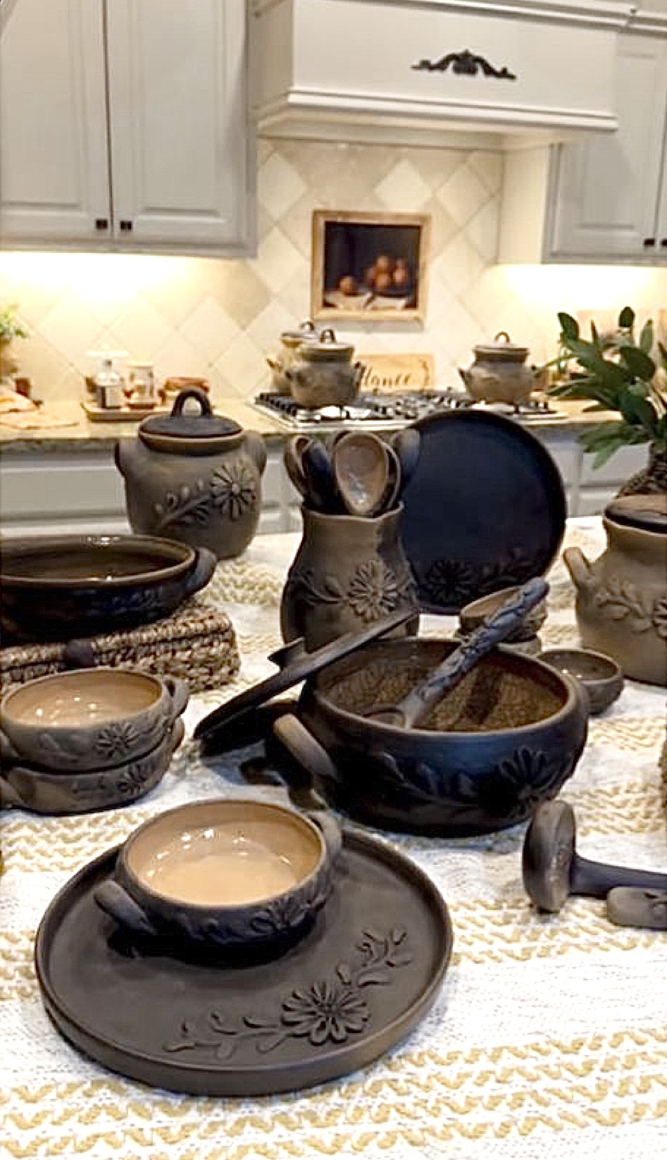 Kitchen countertop with various ceramic bowls, utensils, and a plant, with cabinets and a stove in the background.