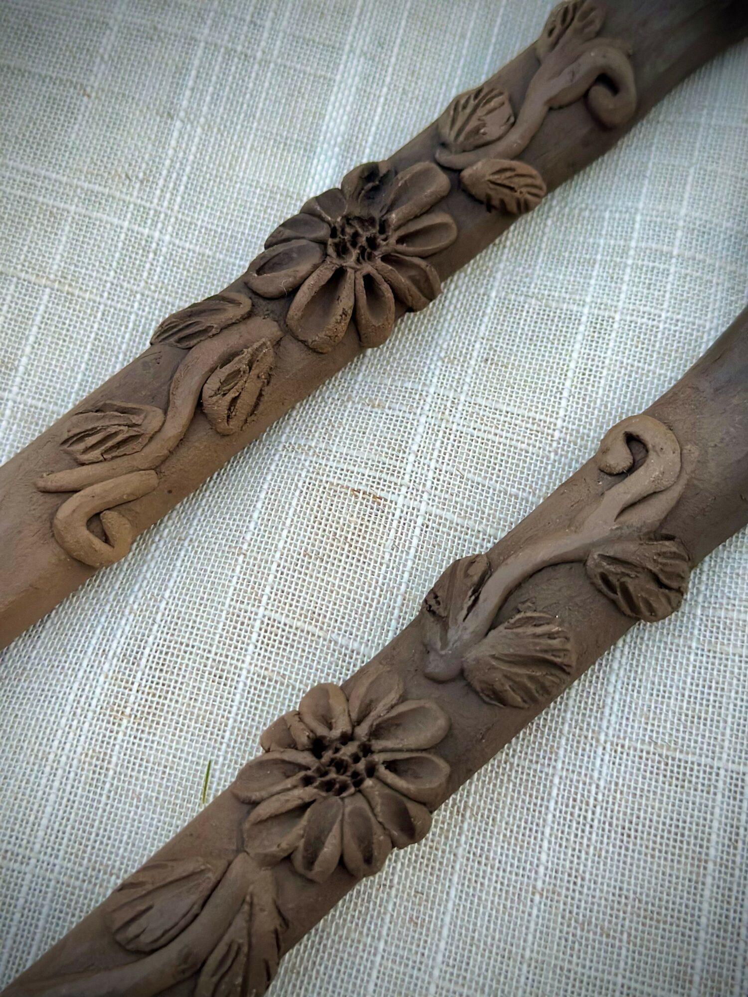 Two brown decorative objects with floral and leaf patterns on a light fabric background.