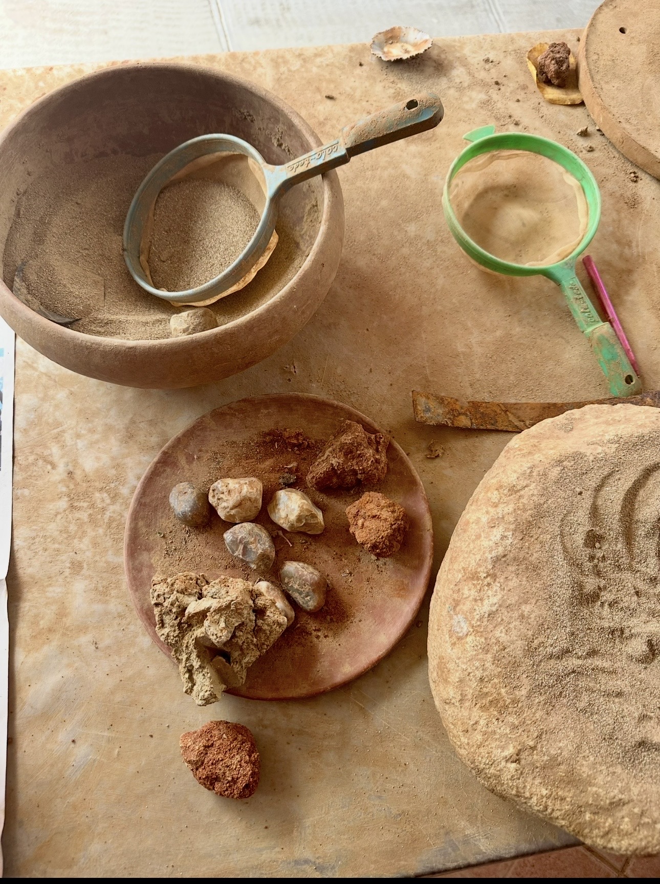 Various stones and rocks on a wooden surface with a bowl, a green-handled tool, and a round object.
