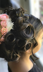 Close-up of a woman's hairstyle with styled curls and floral accessories, partially showing her face and shoulder.