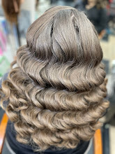 Back view of long, wavy, silver-gray hair with soft curls, in a busy indoor setting.