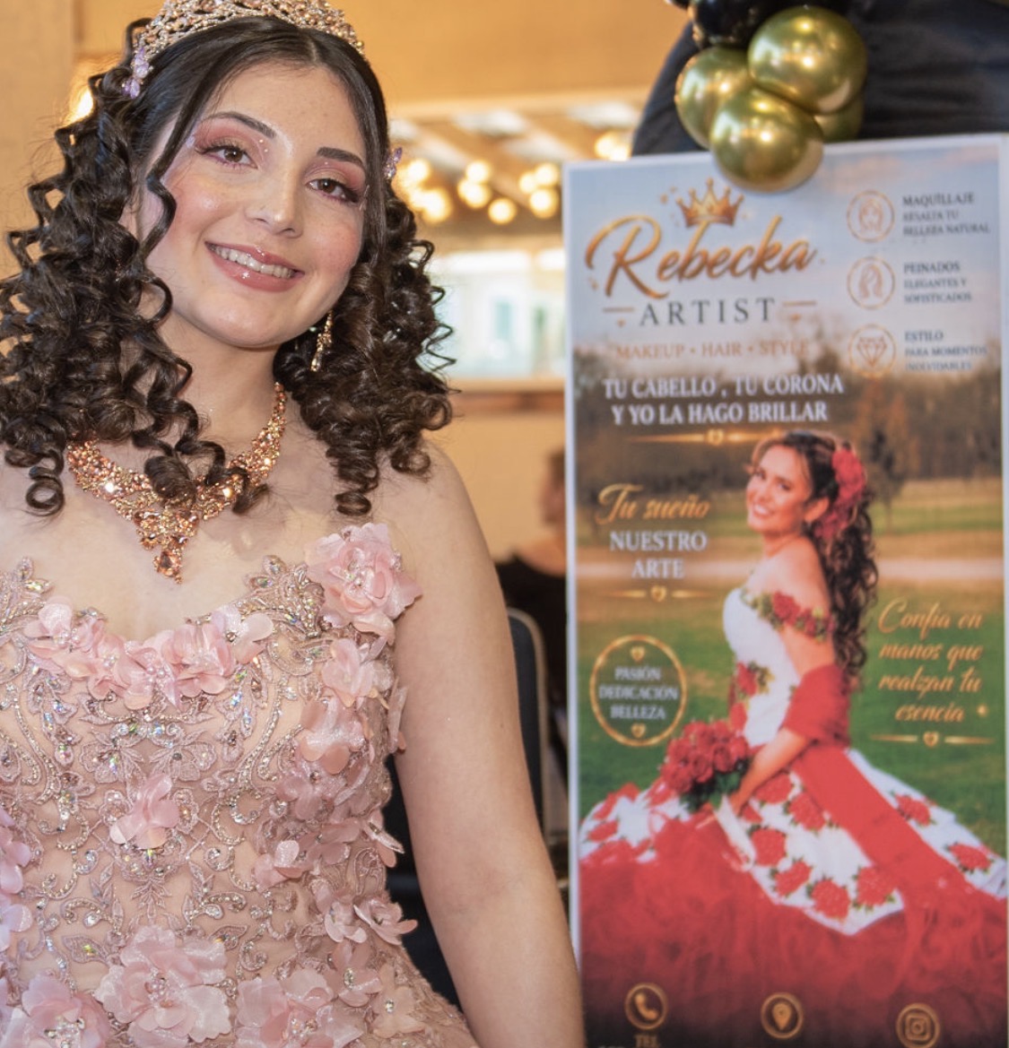 Young woman with curly hair in a pink floral dress smiling, standing next to a promotional poster for Rebecka, an artist, at an event.