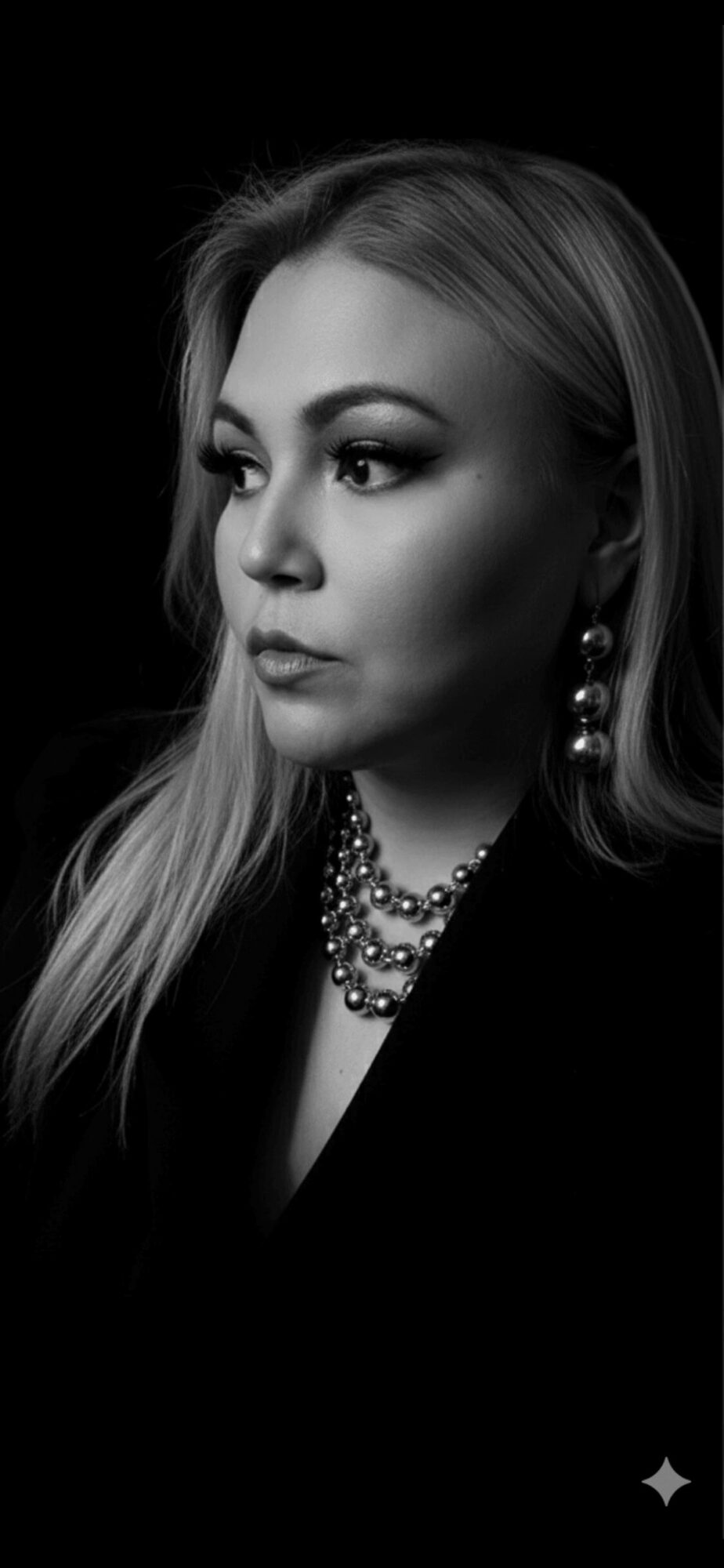 Woman with long hair, wearing earrings and a necklace, looking to the side, in black and white.
