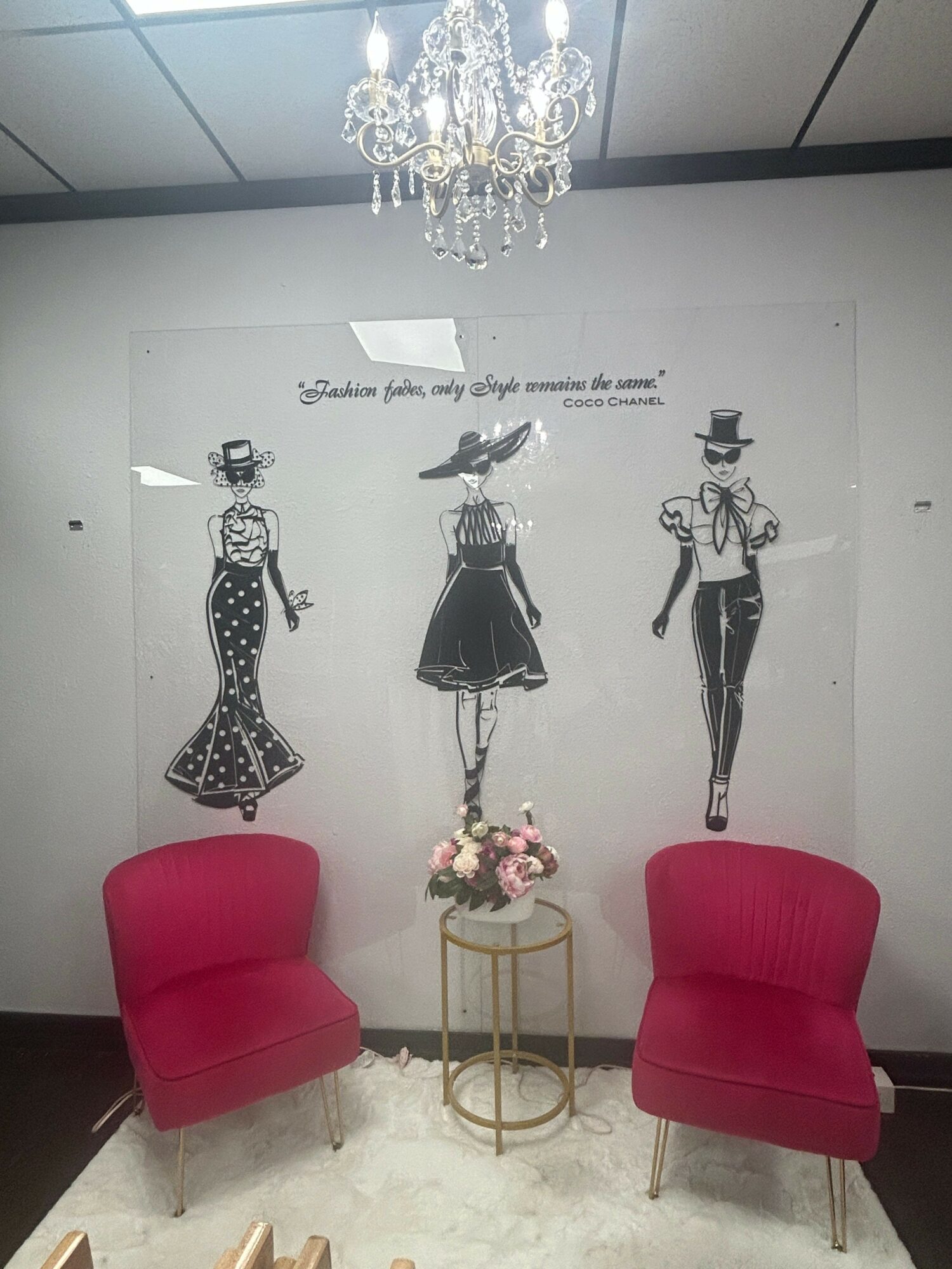 Wall with fashion illustrations, two red chairs, and a chandelier. The wall has three black and white fashion sketches, with a small table holding flowers.