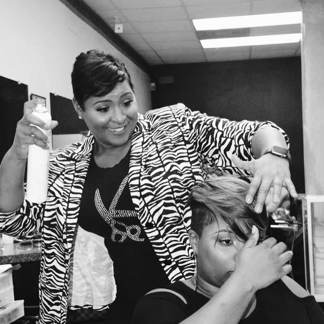 Two women in an office, one smiling and holding a drink, the other adjusting her hair, both in casual attire.