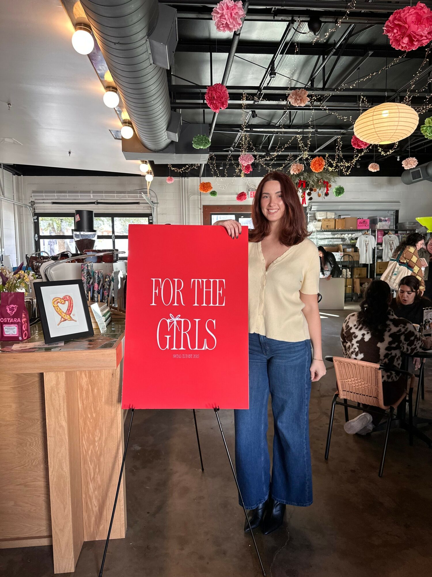 Woman standing near a red sign that reads 'Vote for the Girls' inside a decorated space with flowers and lights.
