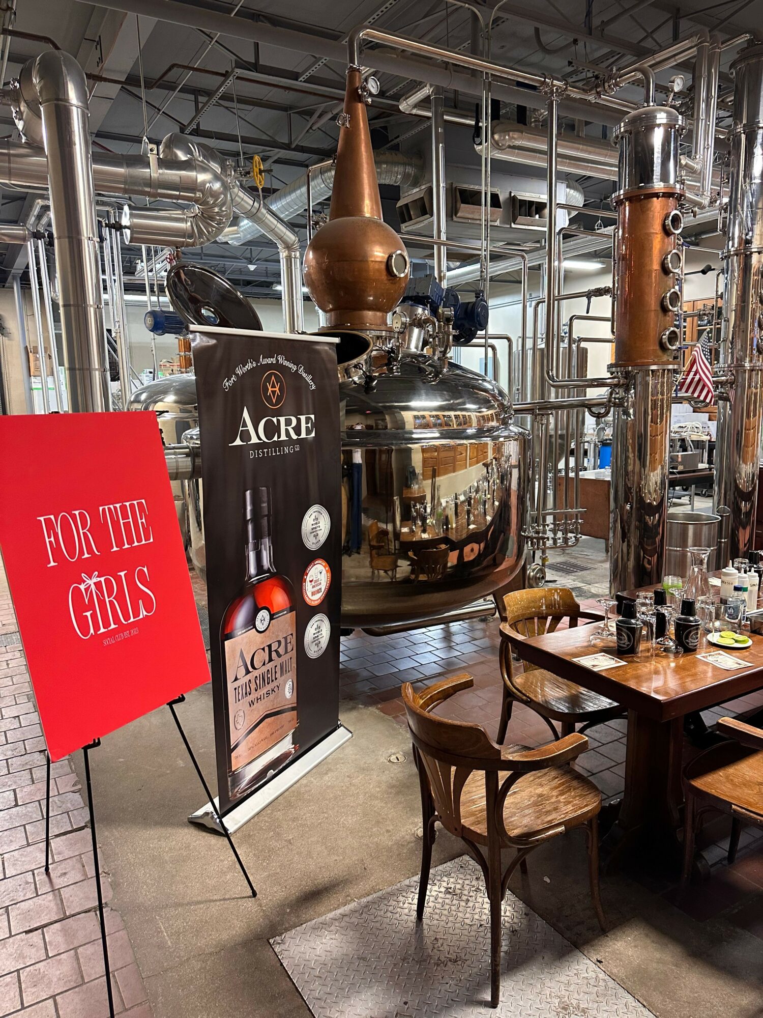 Barrel and distillation equipment in a distillery with a sign for Four Roses whiskey and a promotional stand for whiskey tasting.
