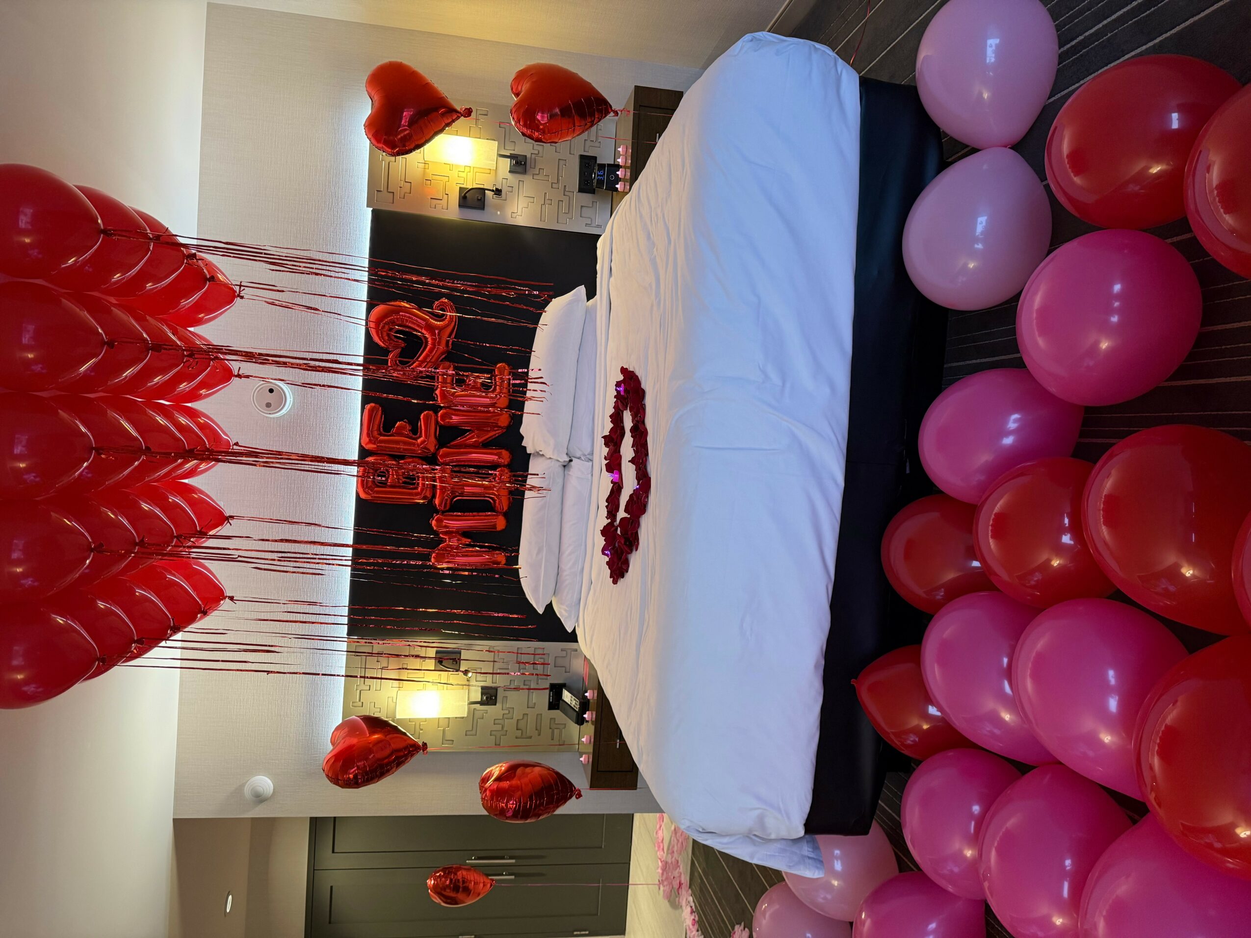 Valentine's Day decorated table with balloons, hearts, and a 'Be Mine' sign, set for a celebration.