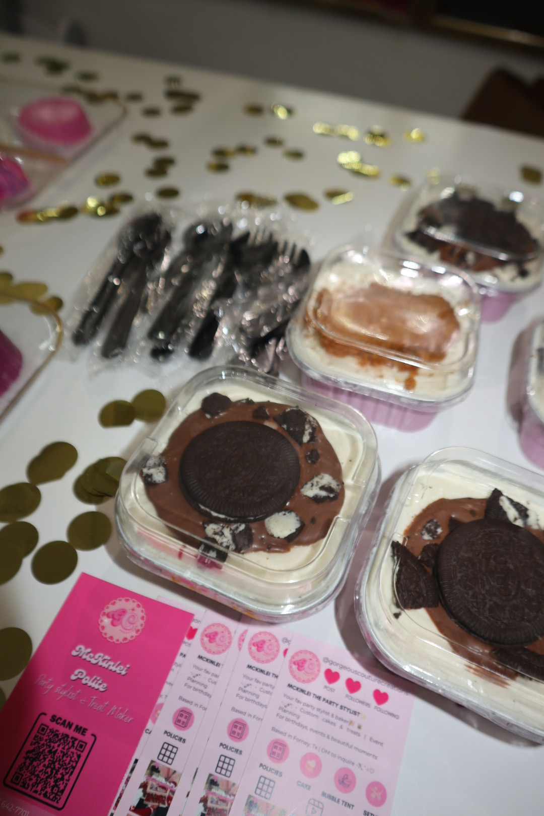 Assorted desserts including cookies and chocolates on a table with gold confetti and pink paper, viewed from the side.