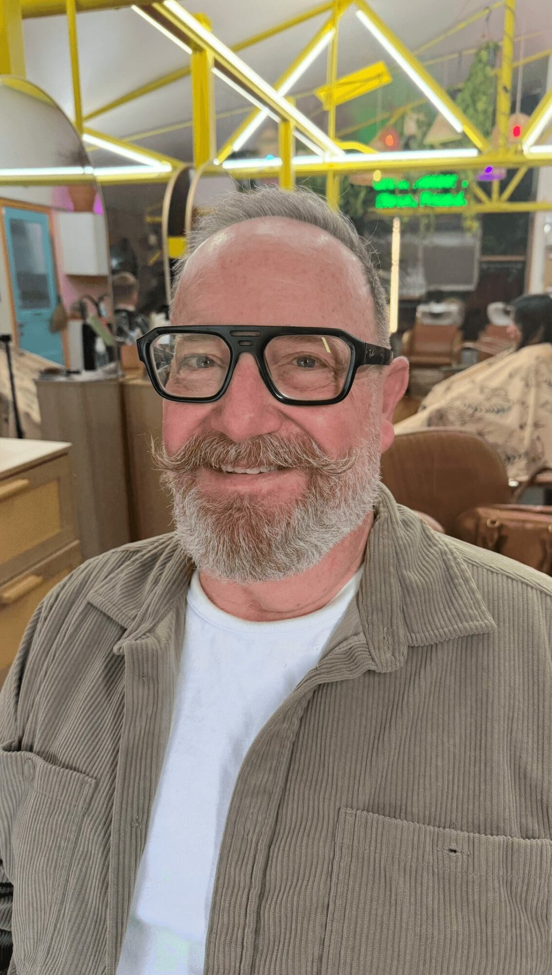 Man with glasses and a beard smiling in a lively indoor setting with colorful lighting.