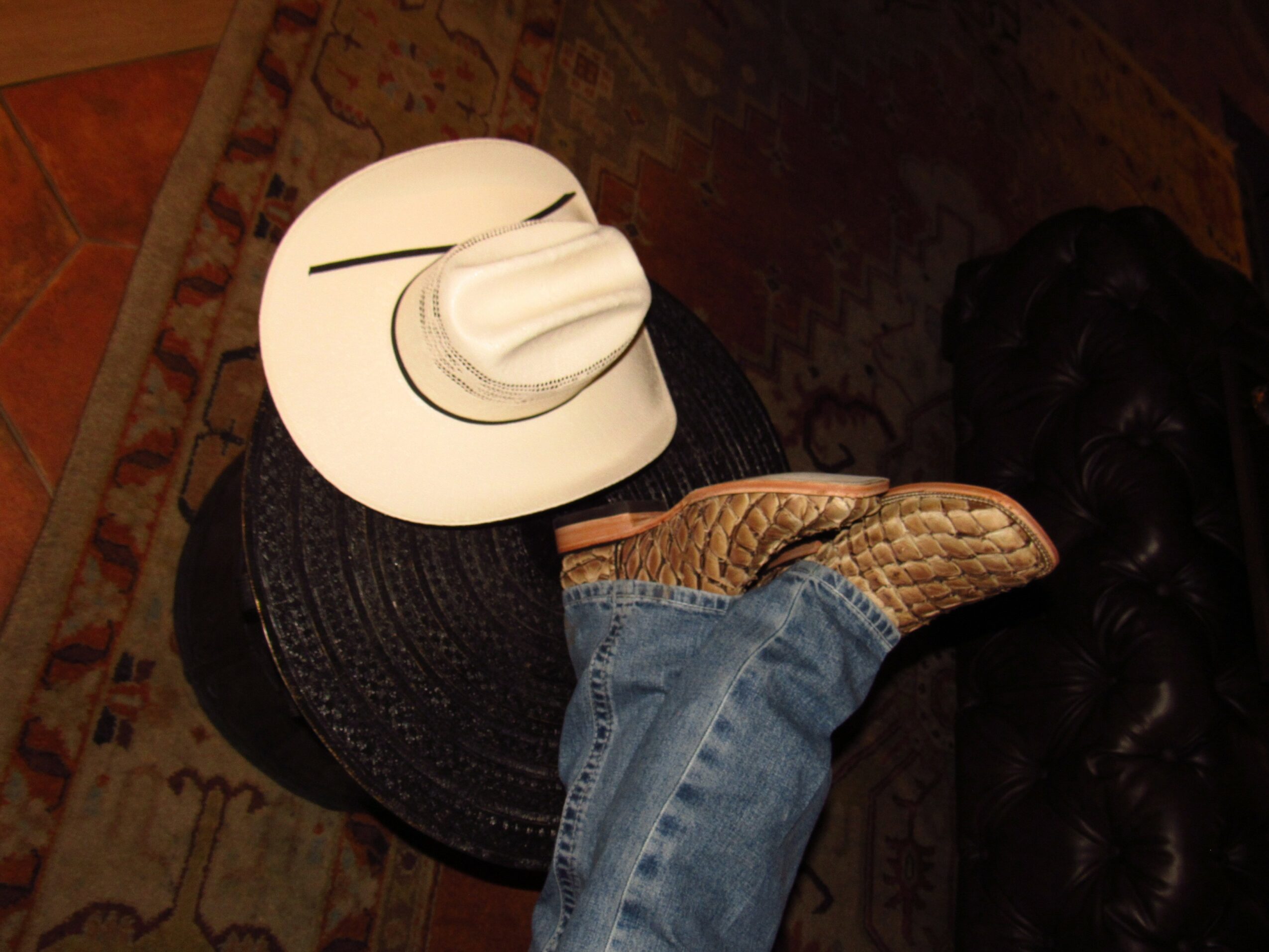 Cowboy hat, sunglasses, and boots on a table, with a person wearing jeans and boots nearby.