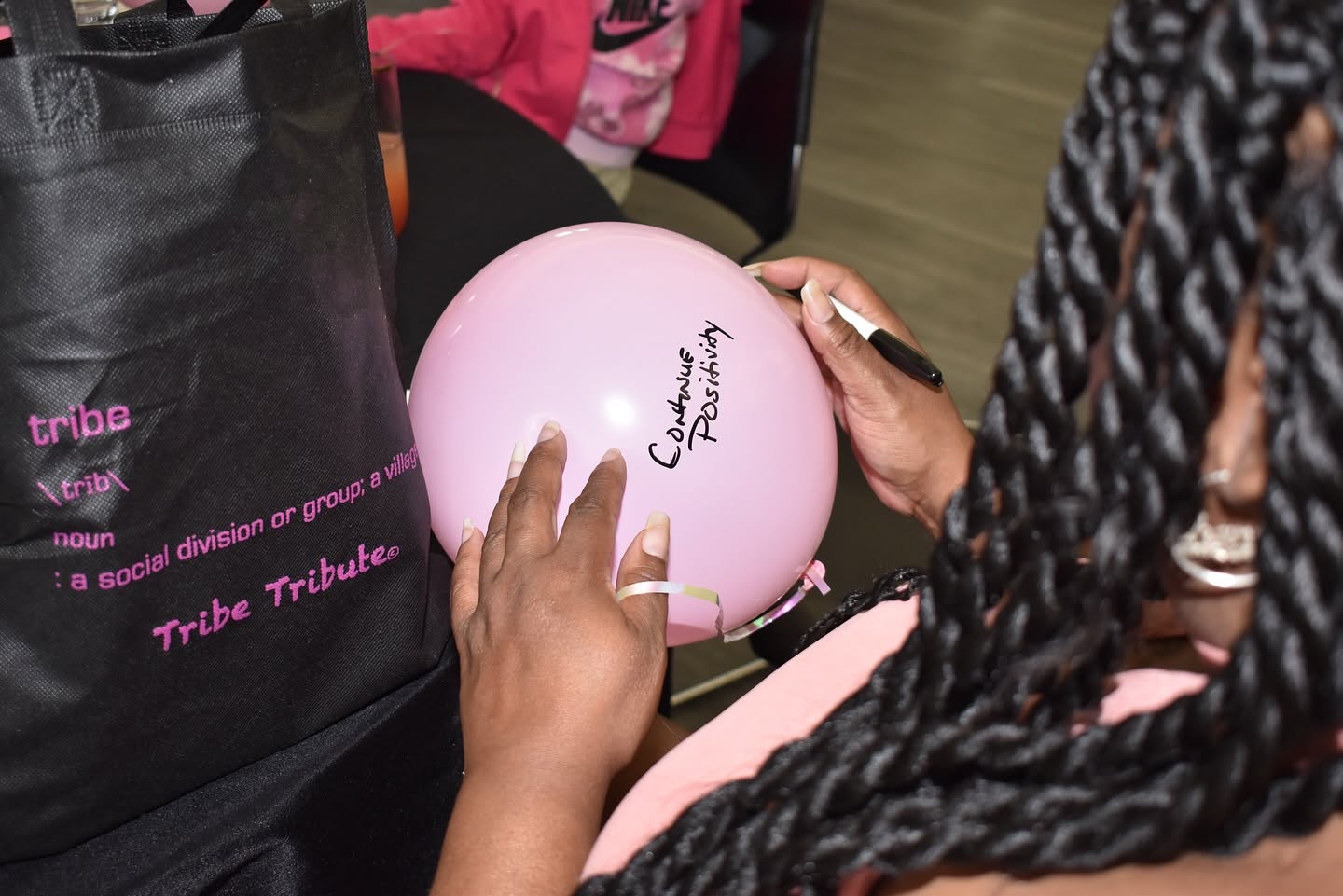 Person holding a pink balloon with a signature, sitting at a table with a black bag nearby.