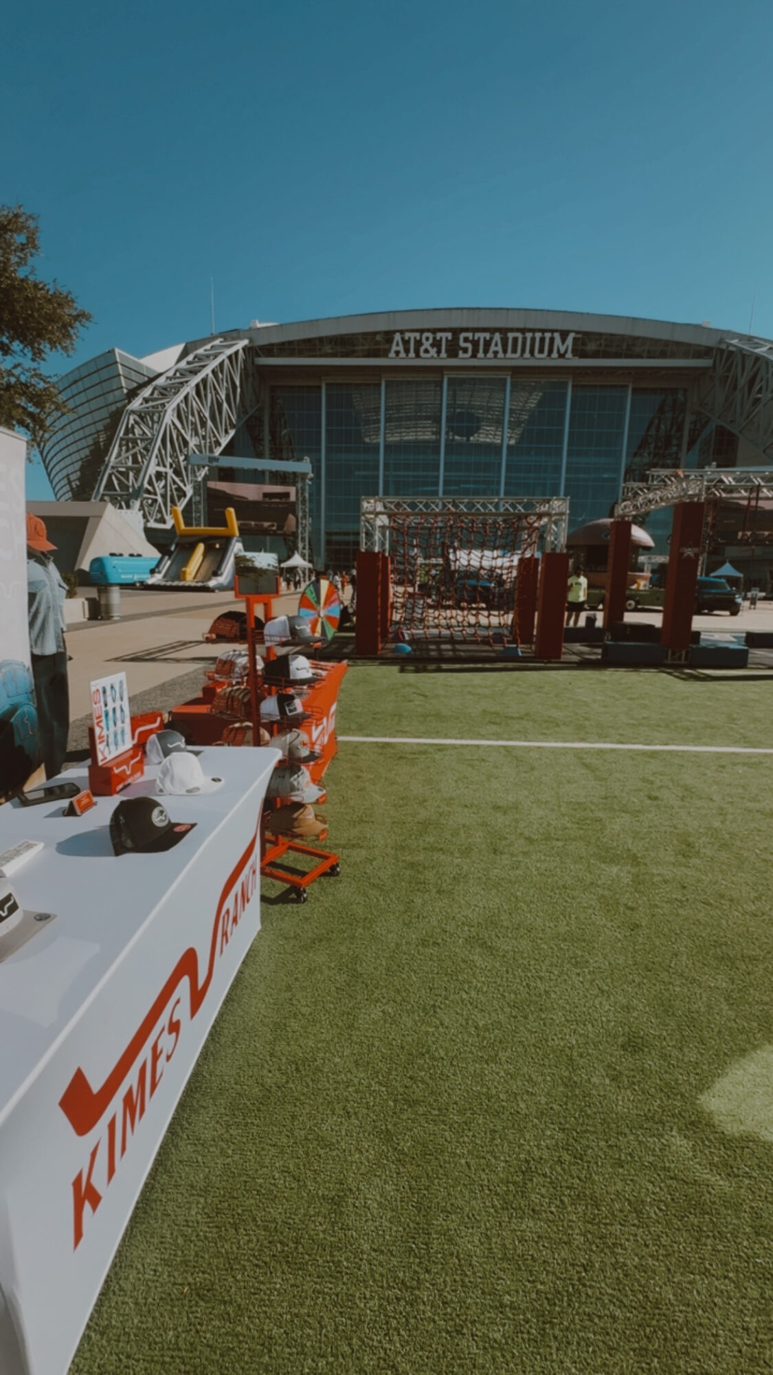 Outdoor scene with a large stadium in the background, tables with items, and a grassy area in the foreground.