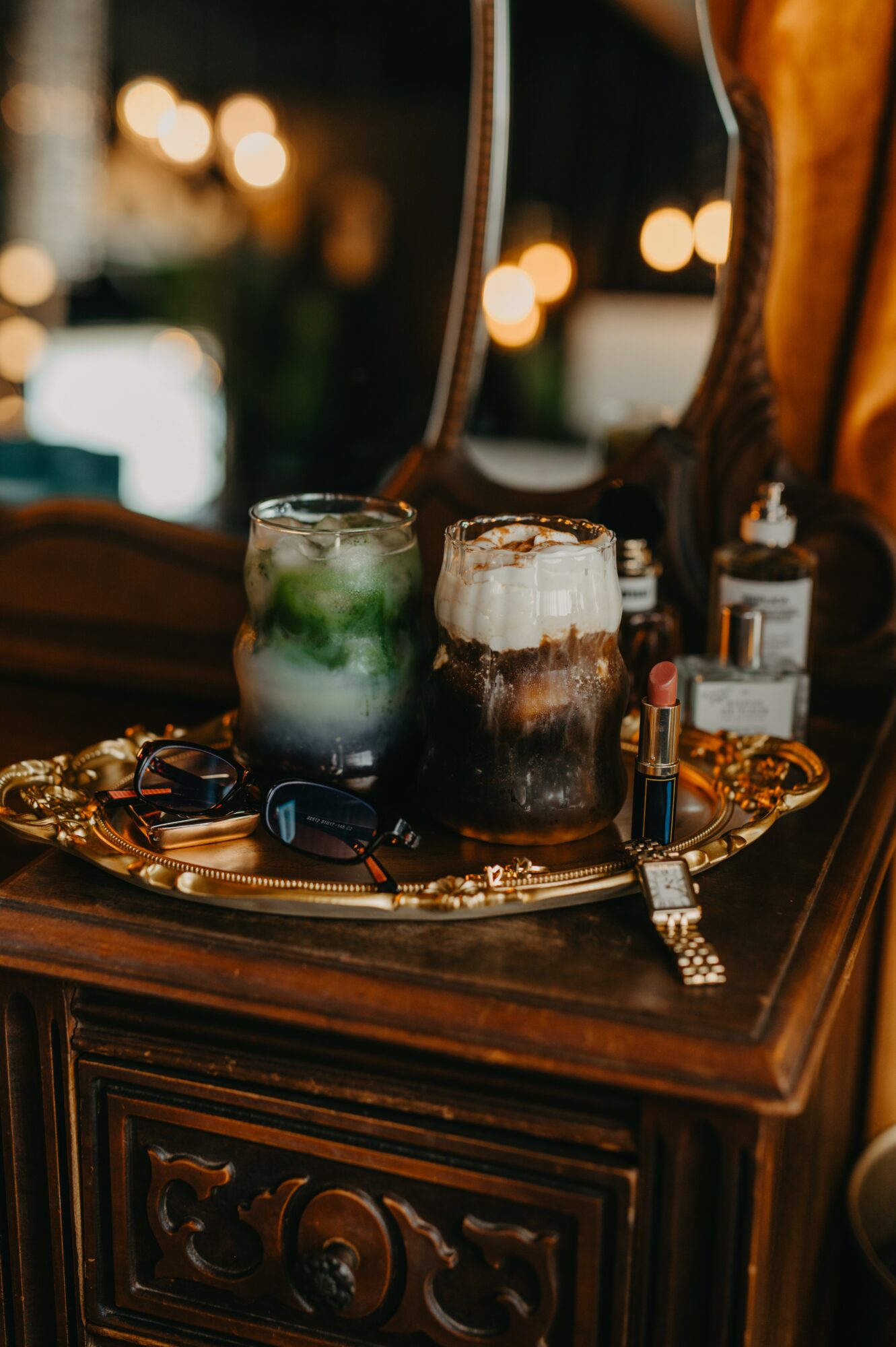 Two colorful drinks on a decorative tray on a wooden surface, with a blurred background of warm lights.