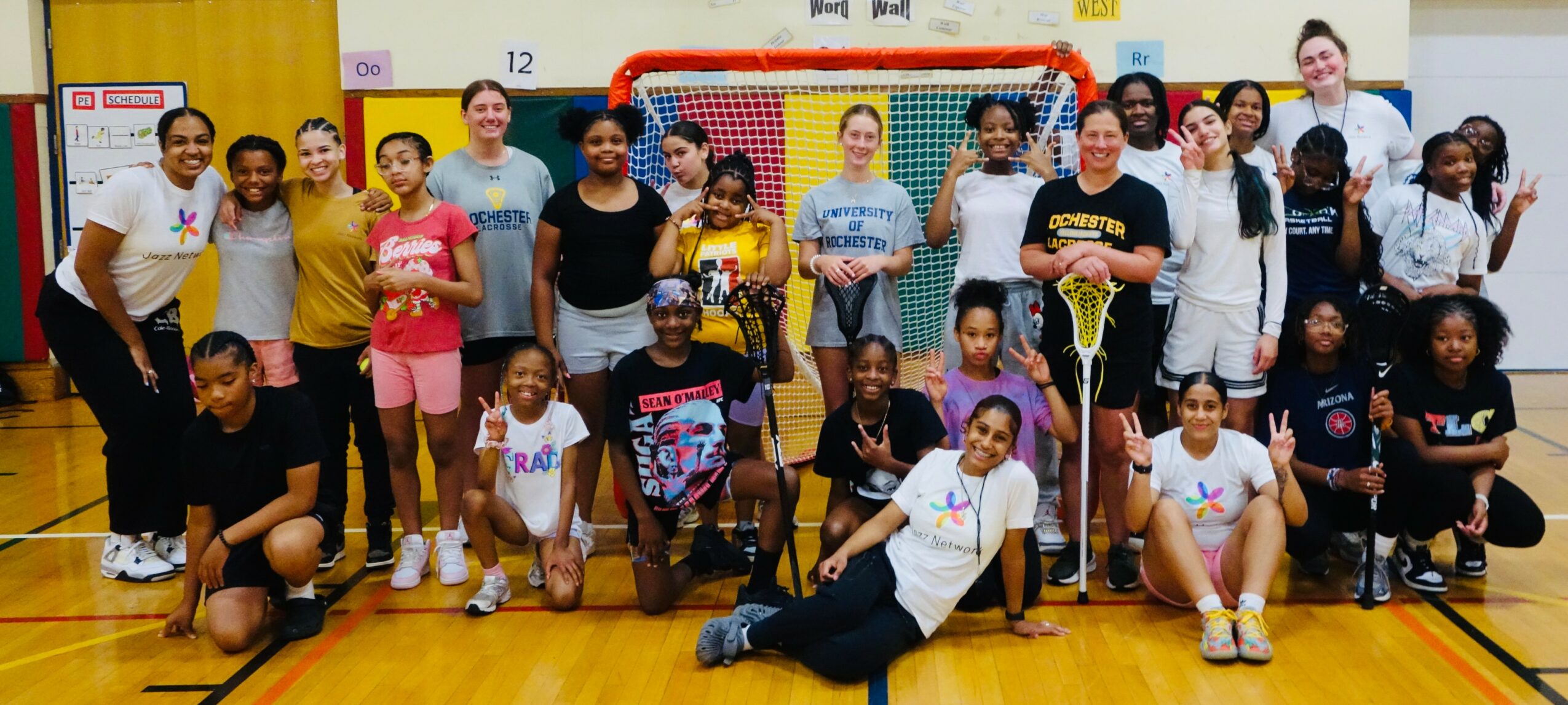 Group of children and adults in a gymnasium, some holding sports equipment, smiling for a group photo.