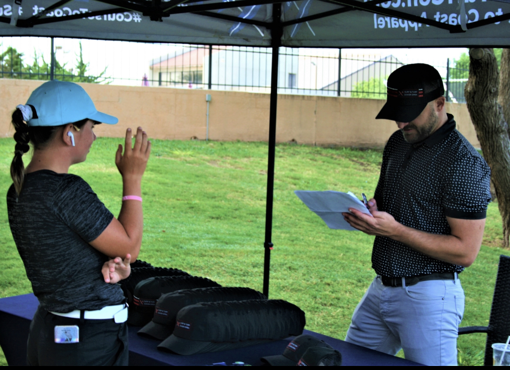 Two people under a canopy, one with a blue cap and the other with a black cap, talking outdoors.