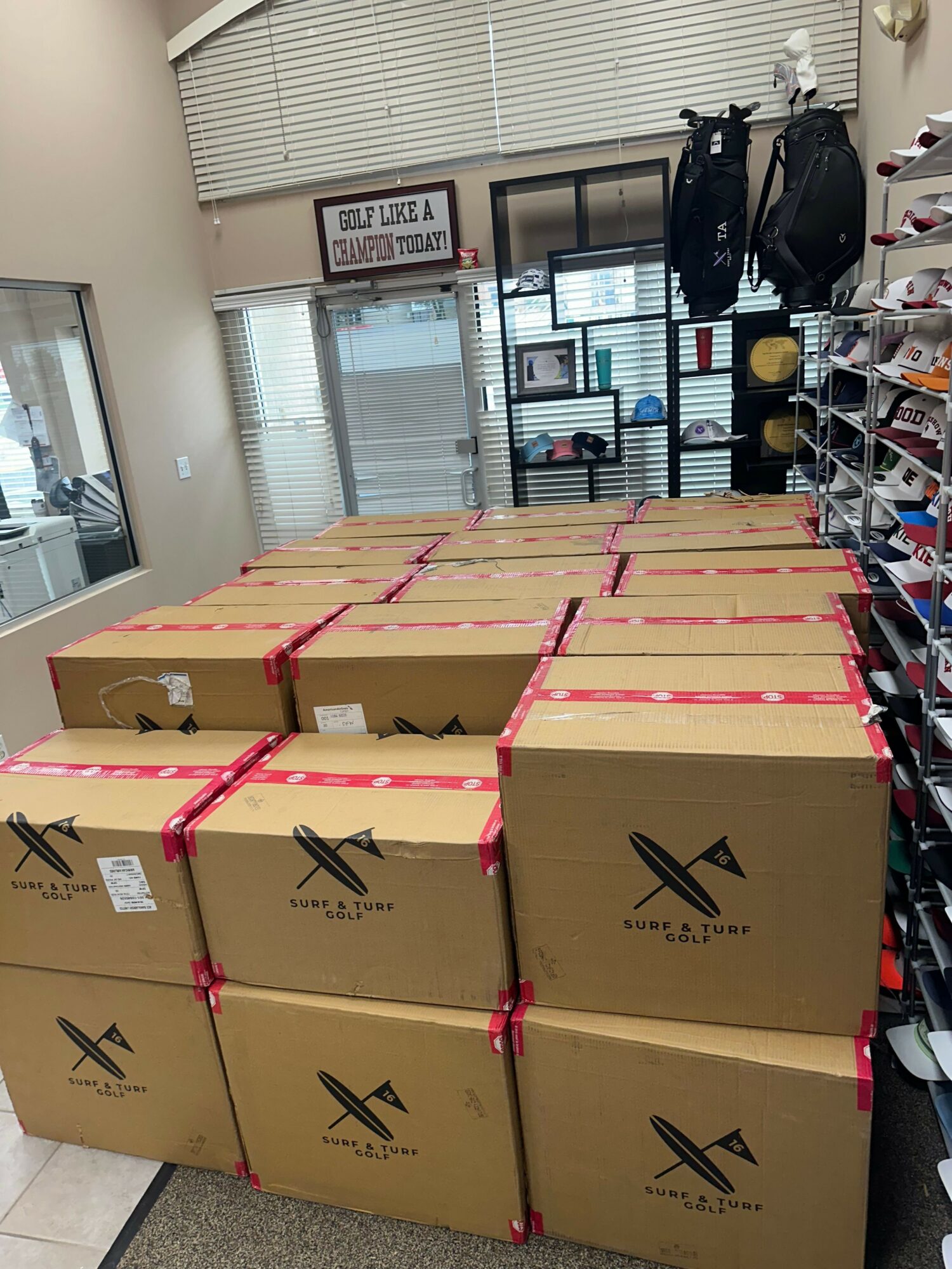 Stacked cardboard boxes with black logo and red straps in a room with shelves and windows.