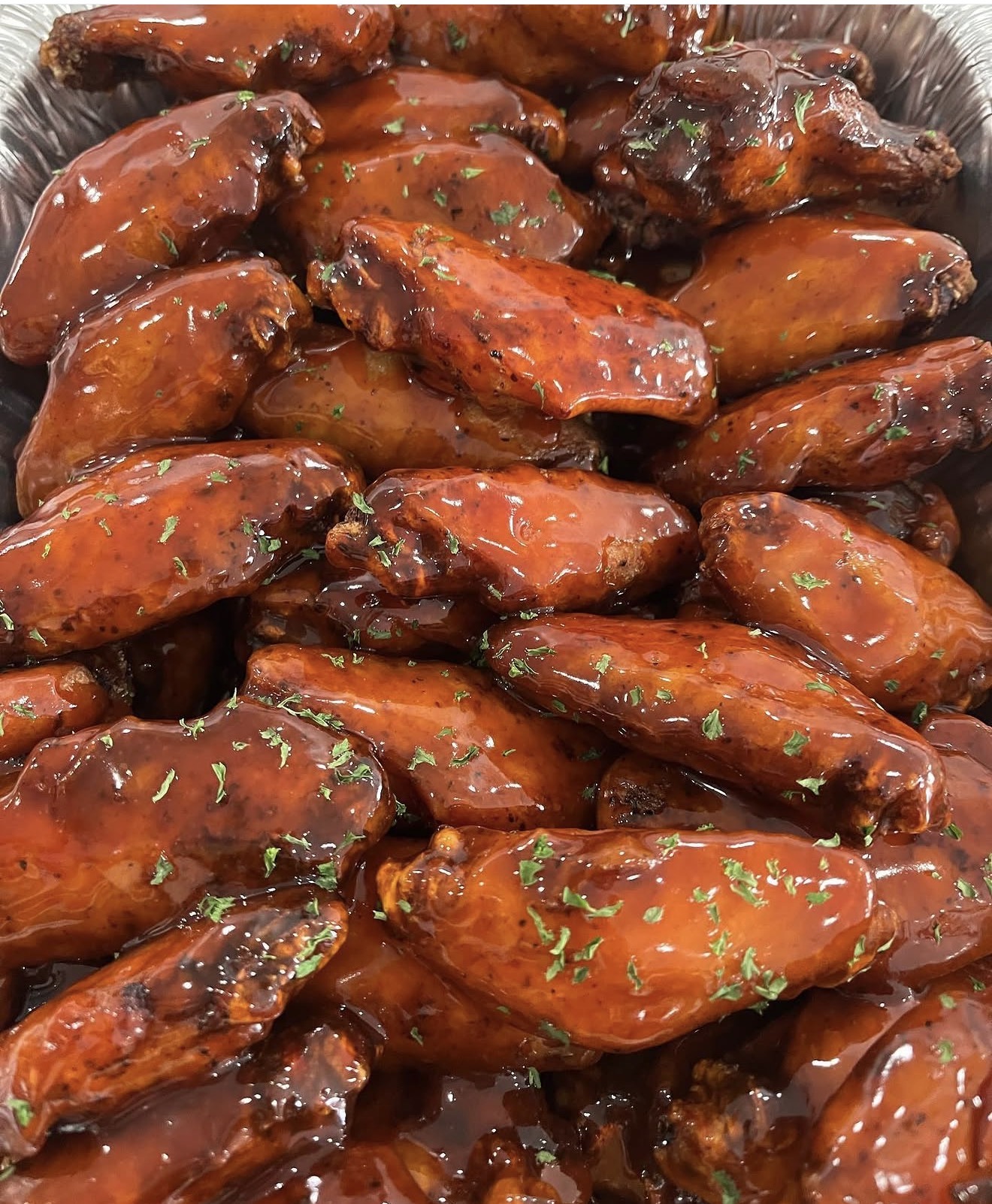 Barbecue chicken wings coated in sauce with herbs, arranged in a tray.