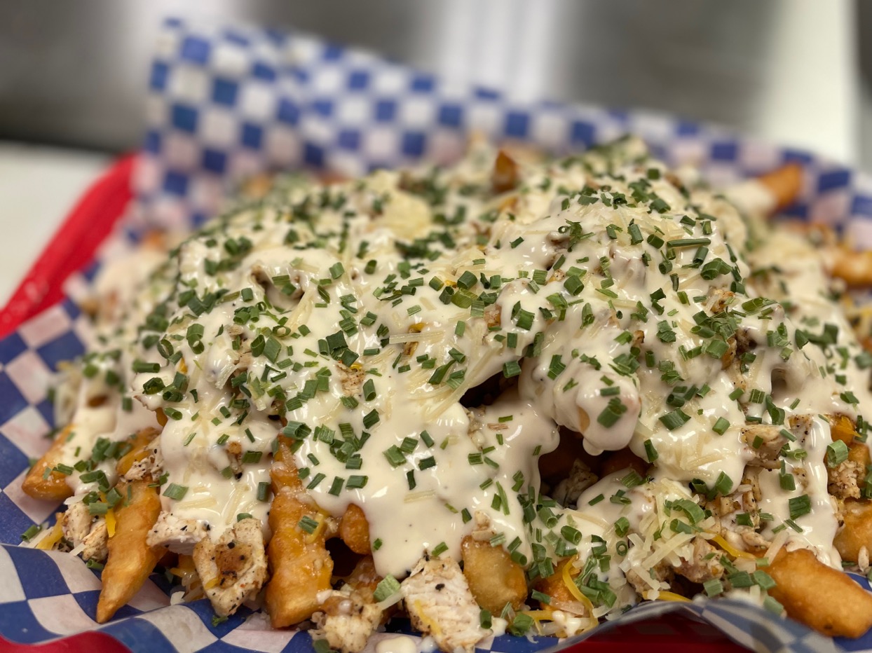 Plate of loaded fries topped with white sauce, chopped chives, and herbs, with a checkered napkin in the background.