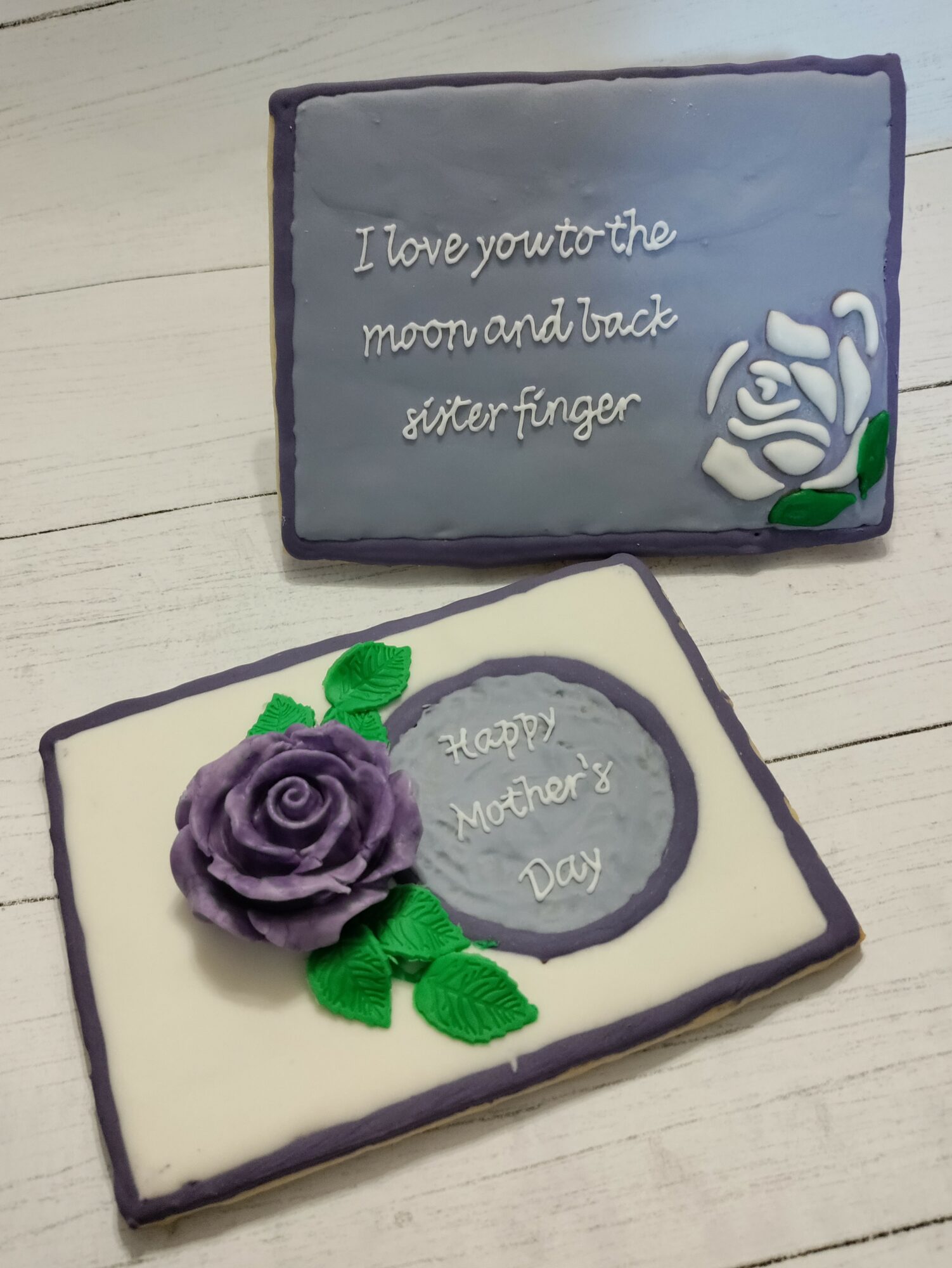 Decorative card with purple rose and green leaves, message for Mother's Day, on a white wooden surface.