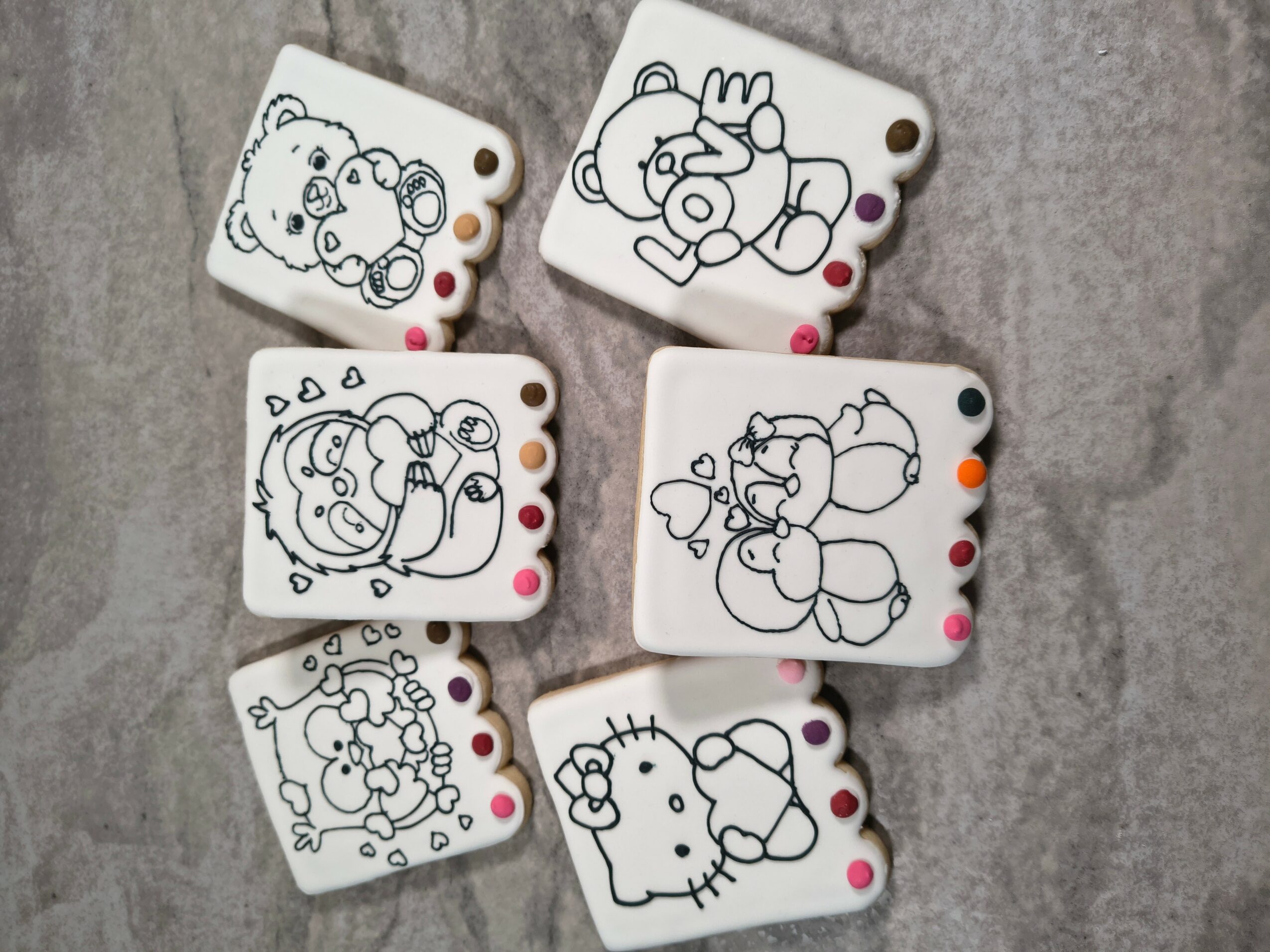 Six small white objects with cartoon character drawings and colored dots, placed on a gray surface.