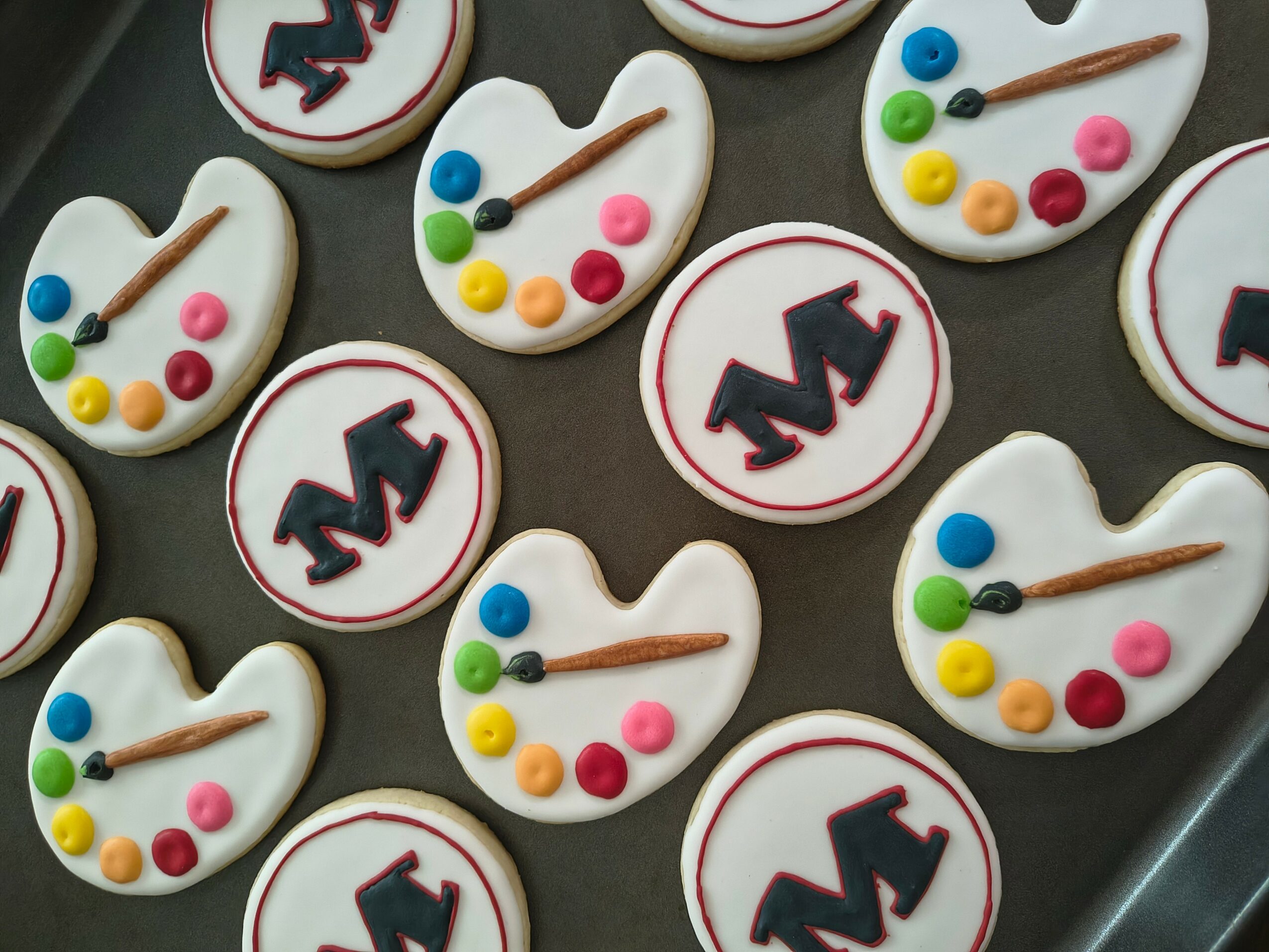 Cookies decorated with paint palettes and logo designs, arranged on a tray, with colorful icing and designs.
