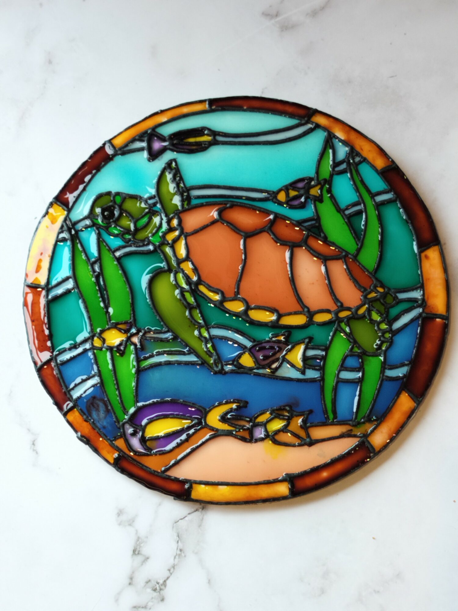 Colorful stained glass turtle surrounded by green plants, with a blue background, in a circular design.