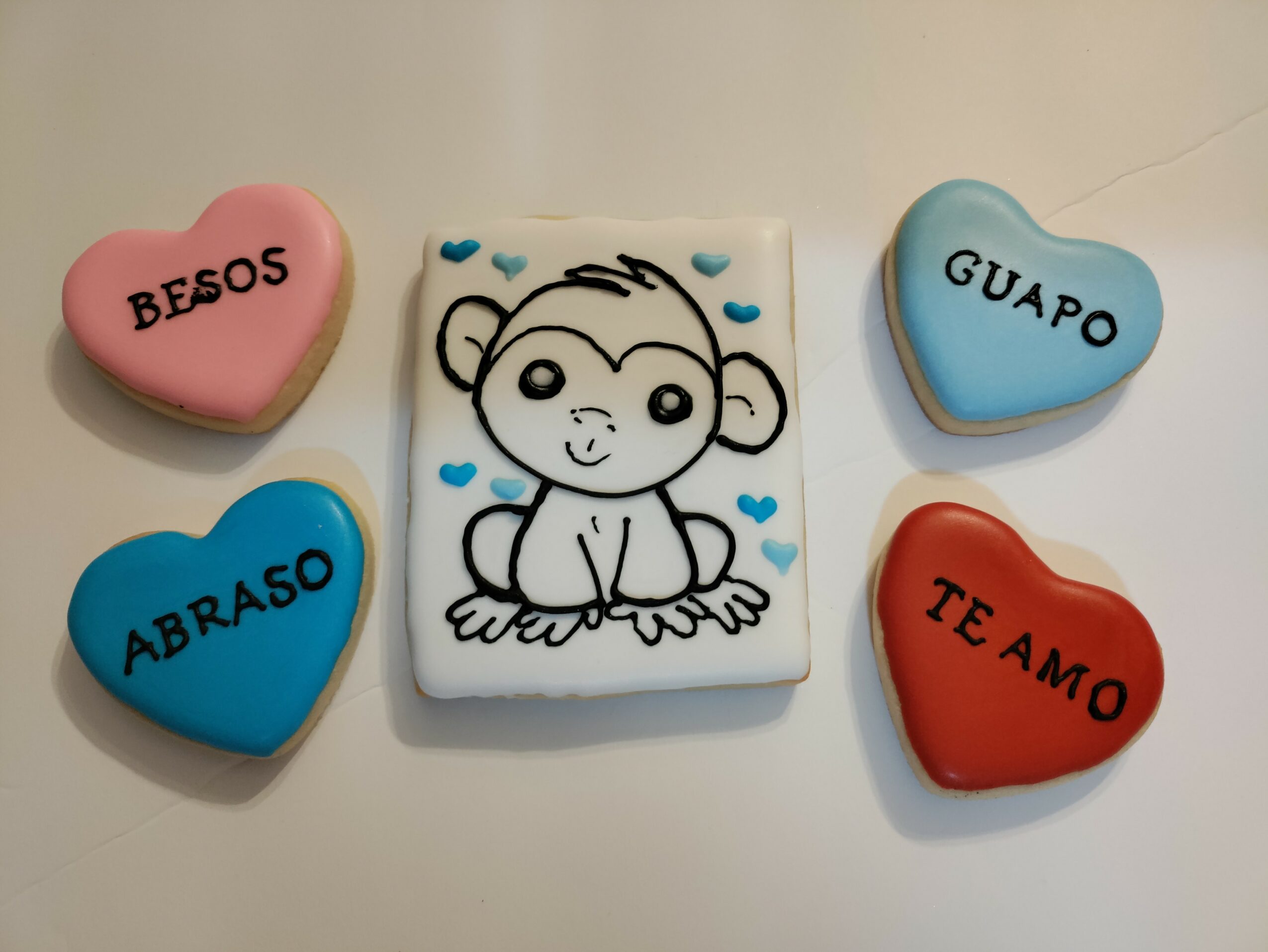 Four heart-shaped cookies and a rectangular cookie with a monkey drawing, on a white surface.