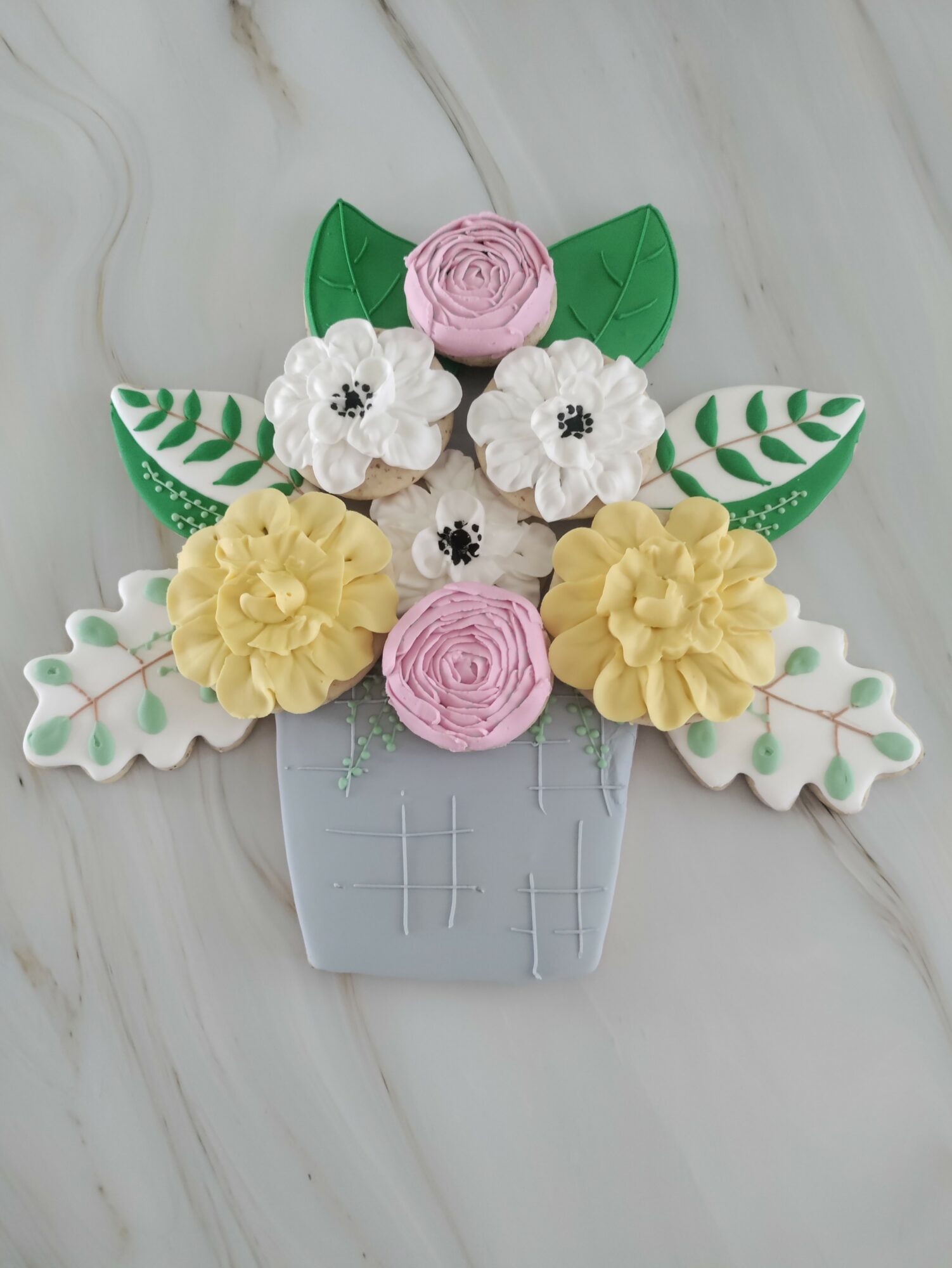 Decorative flower arrangement with pink, white, and yellow flowers in a gray pot, on a light marble surface.