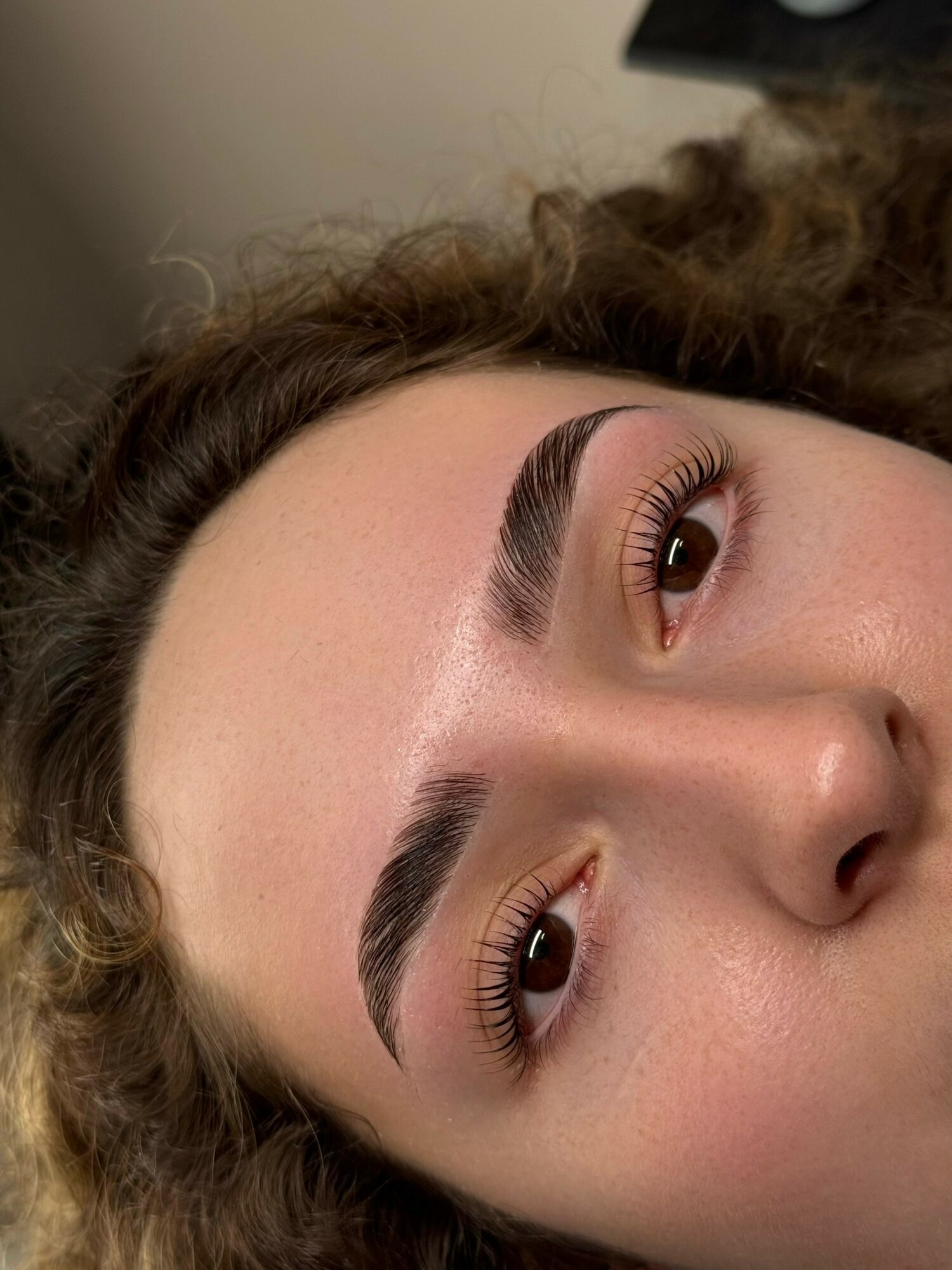 Close-up of a woman's face with well-groomed eyebrows and makeup, lying sideways with her head tilted.