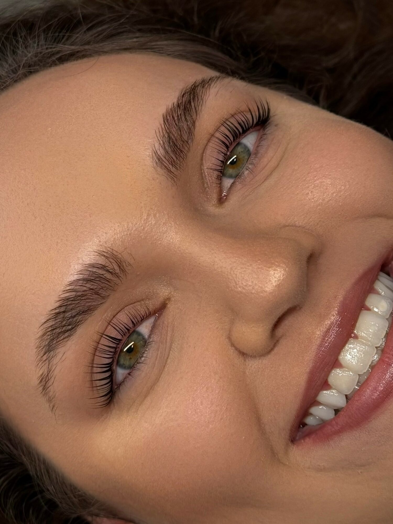 Close-up of a smiling woman's face showing her eyes, eyebrows, nose, and teeth.