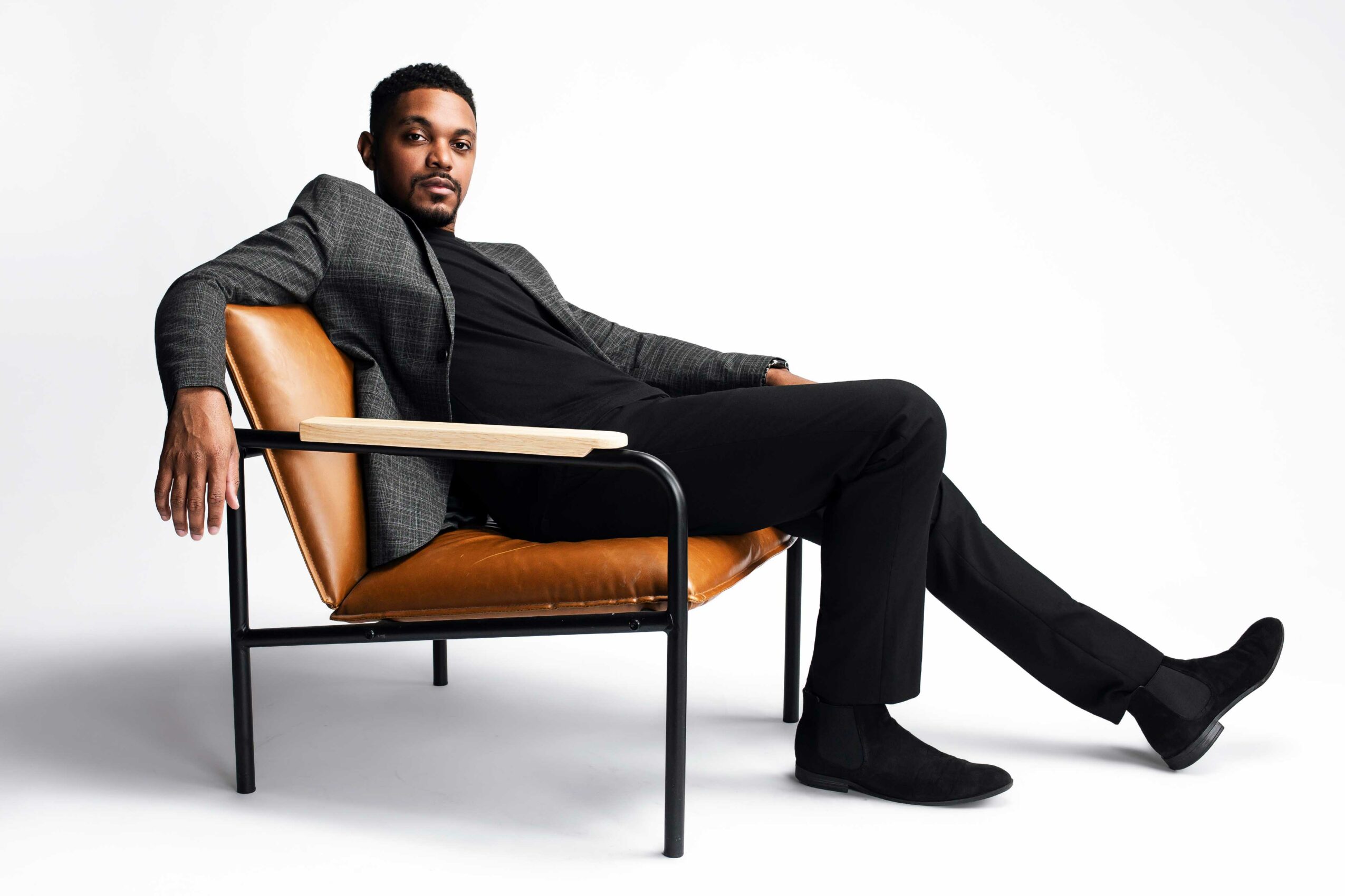 Man in dark suit sitting on a modern chair with a white background.