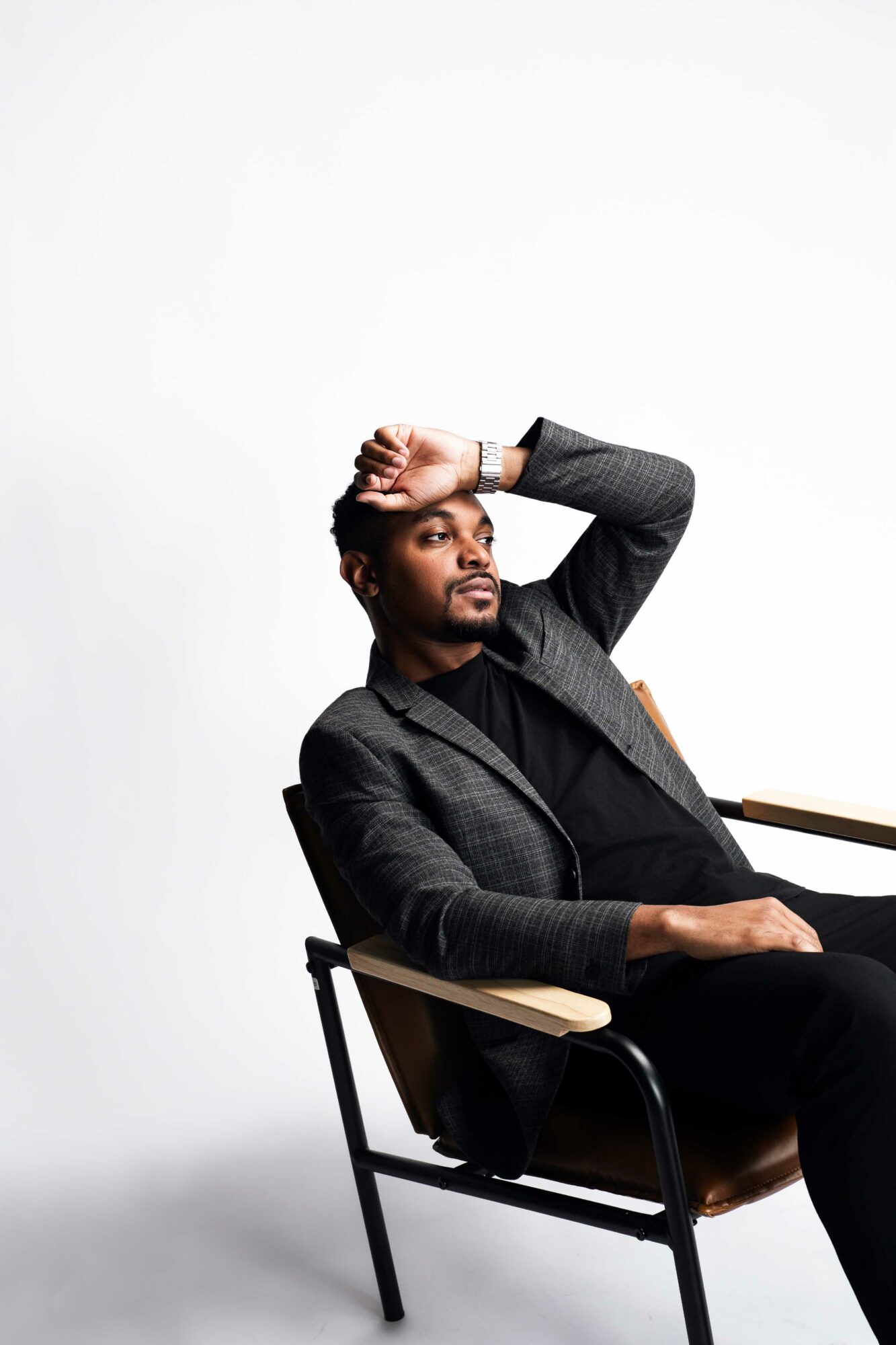 Man sitting in a chair with one arm resting on the armrest and the other hand on his forehead, against a plain white background.