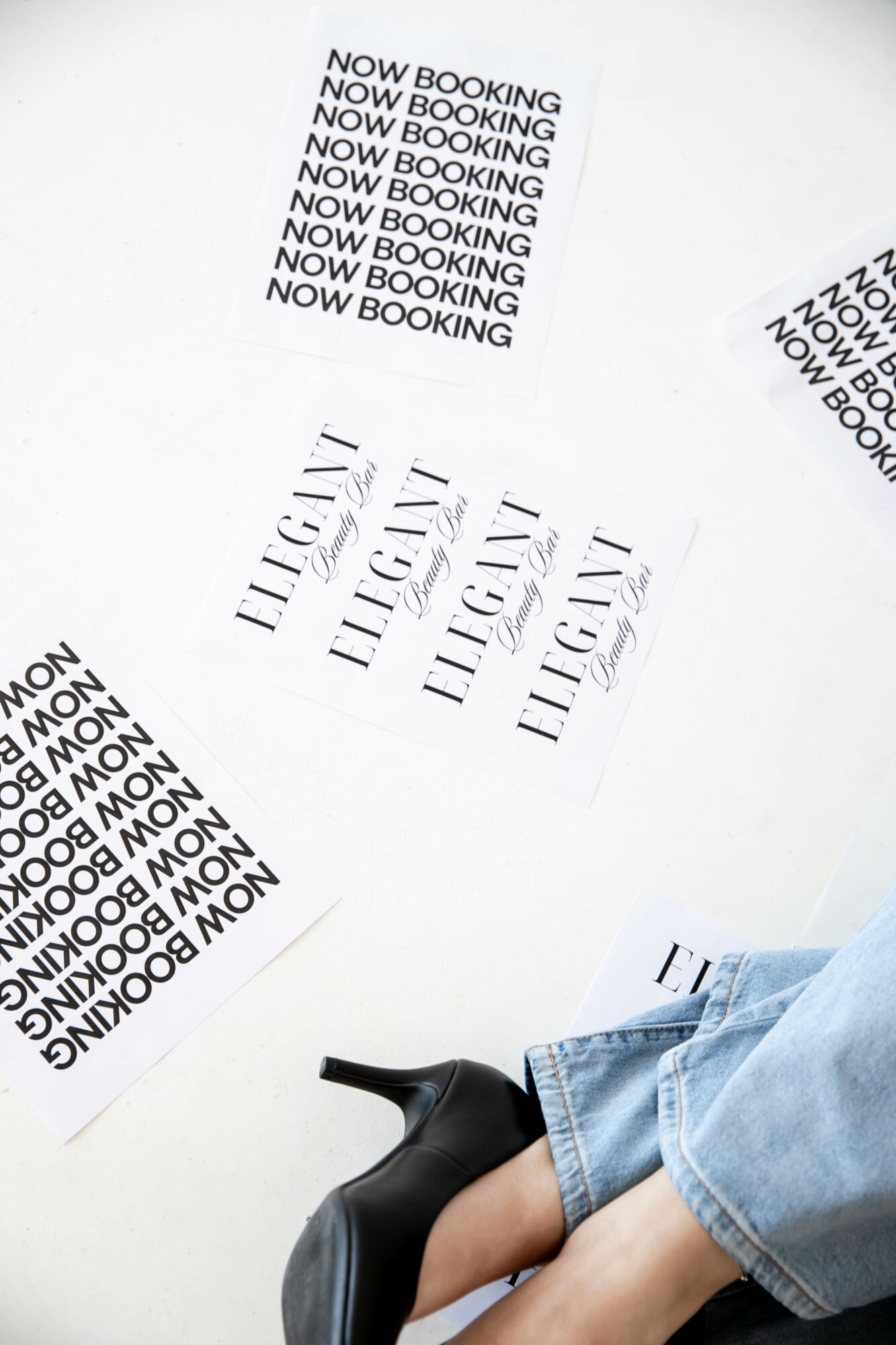 Person's legs in jeans and black shoes, with multiple sheets of paper on a white surface, some with text.