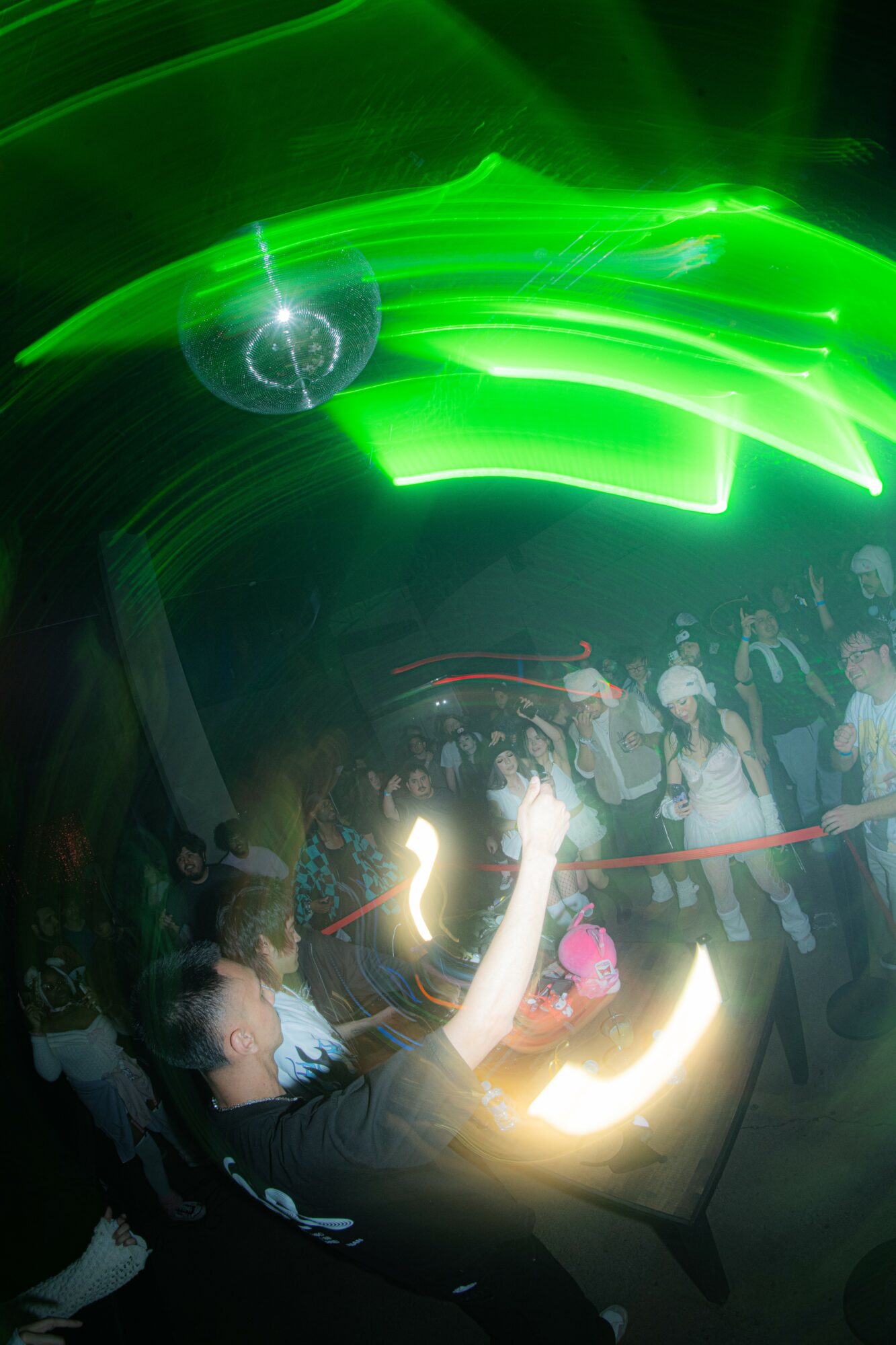 People dancing in a club with green lights and a dark background, some with raised hands, motion blur effects.