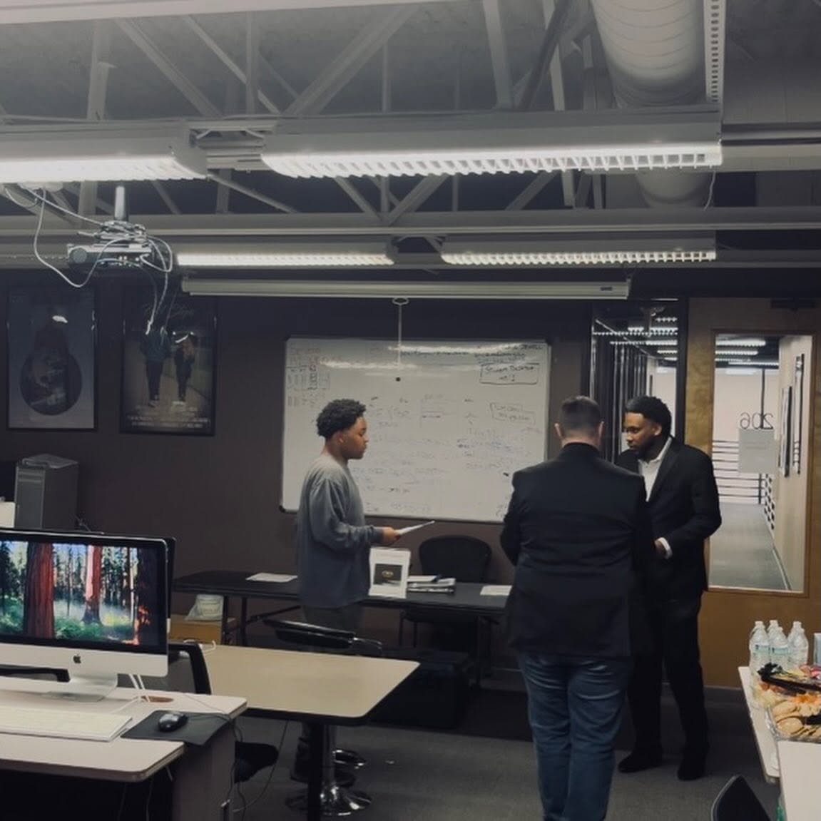 Three people in a meeting room, two men and one woman, standing near a whiteboard, engaged in discussion.