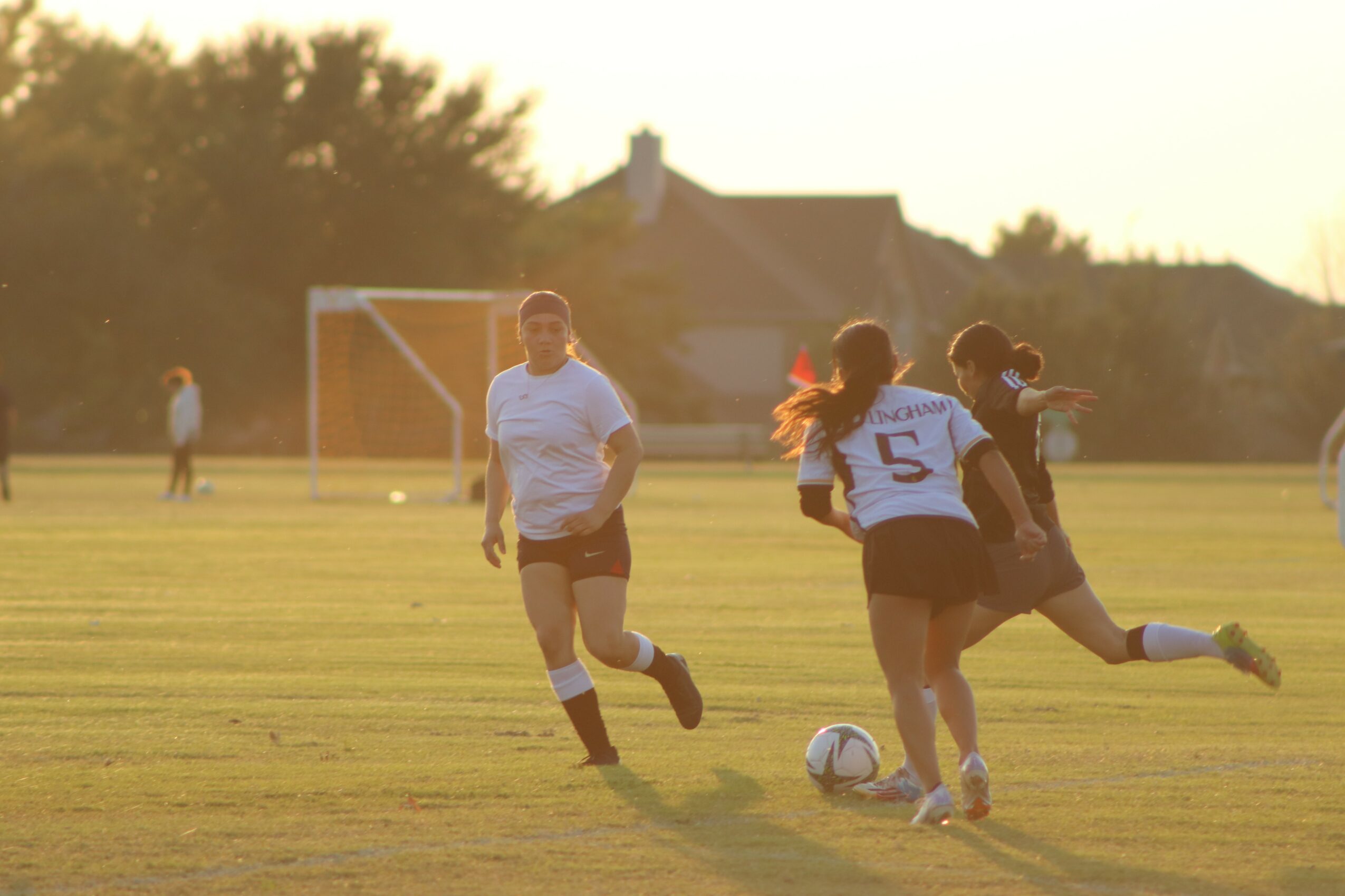 Group of children playing soccer on a field during sunset, with a goalpost in the background.