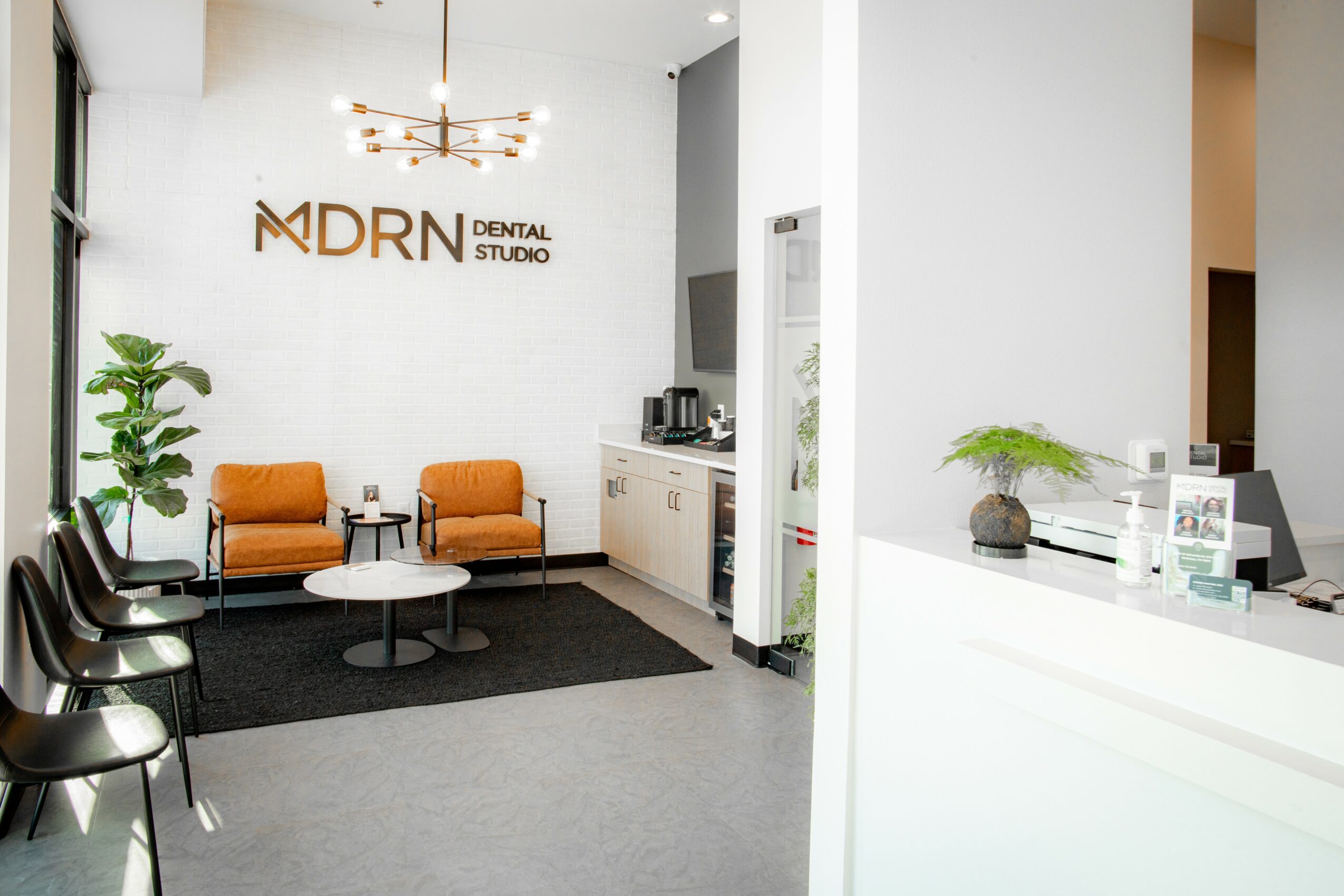 Dental office waiting area with chairs, a small table, and a reception desk, featuring a sign reading 'MDRN Dental Studio'.