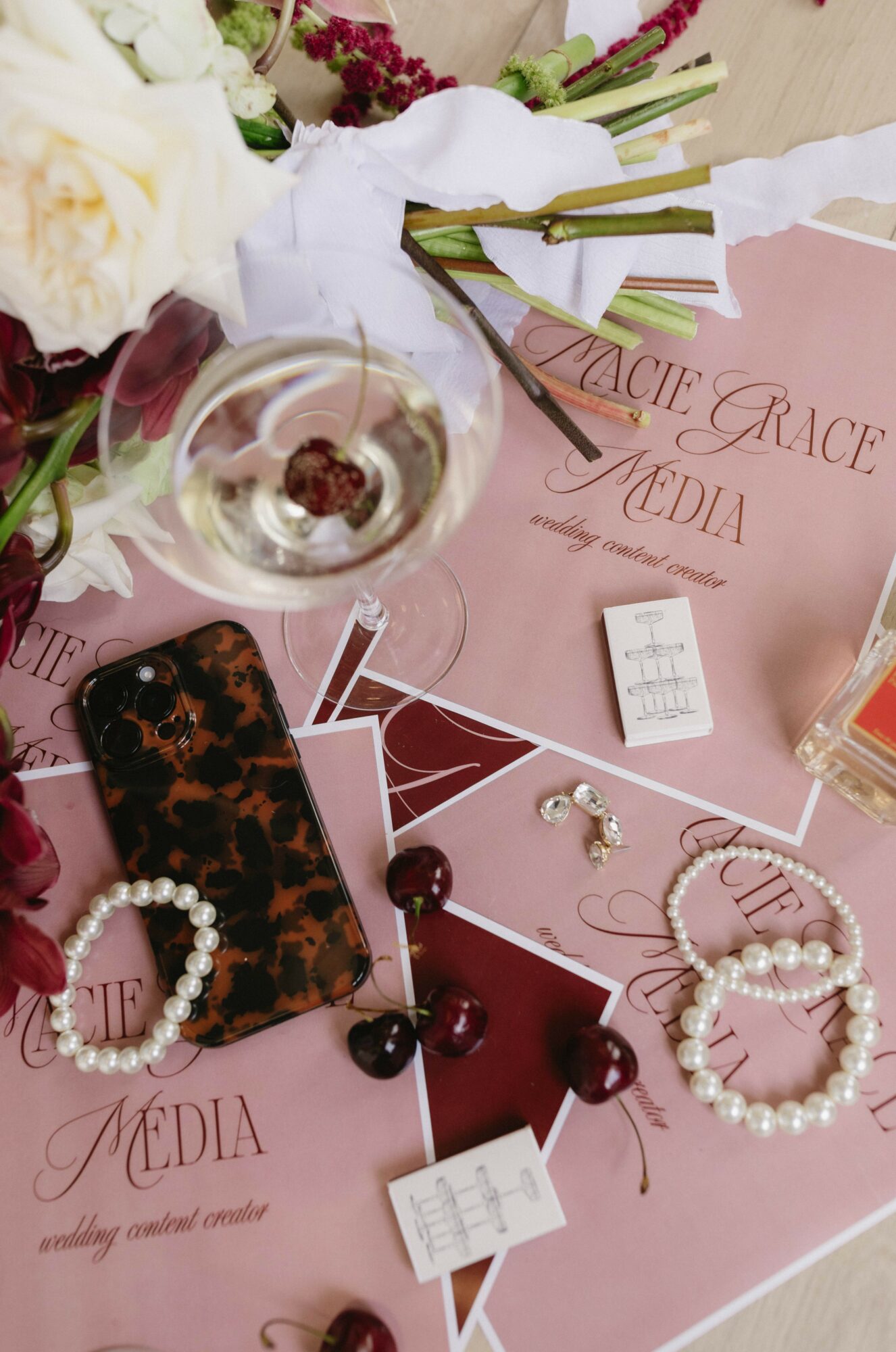 Flat lay of jewelry, a leopard print case, and pink media cards with flowers in background.