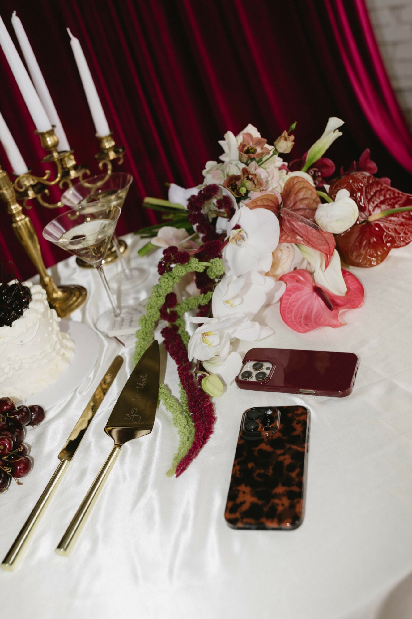 Table with floral centerpiece, candles, and smartphones on white tablecloth, against a red curtain background.