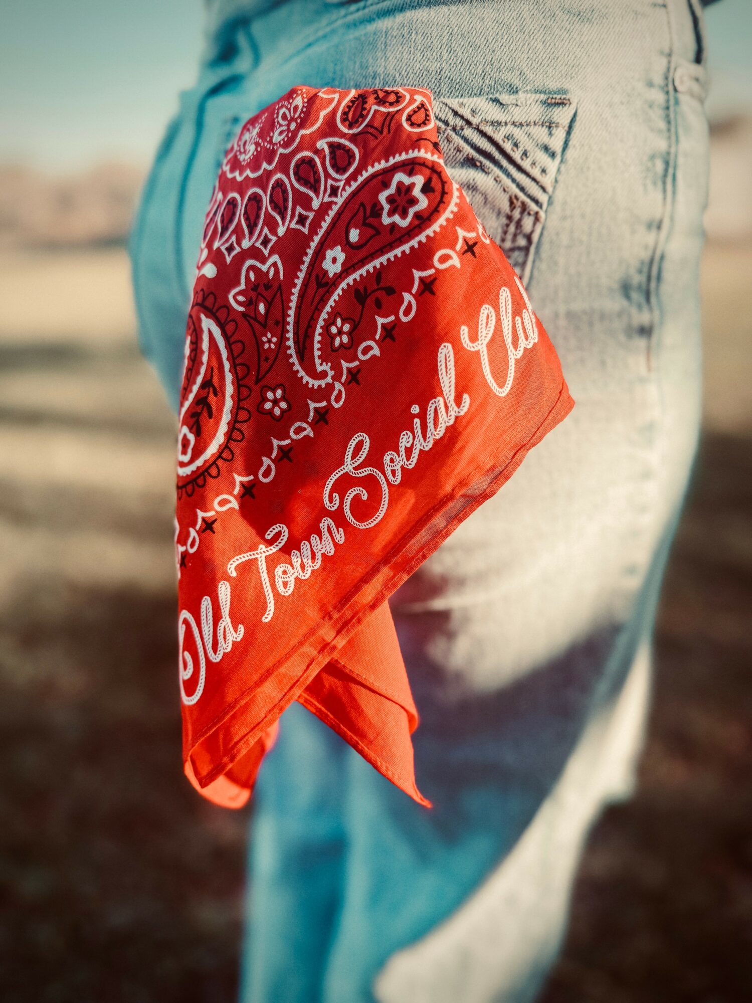 Close-up of a person wearing jeans with a red bandana in back pocket, outdoors, blurred background.