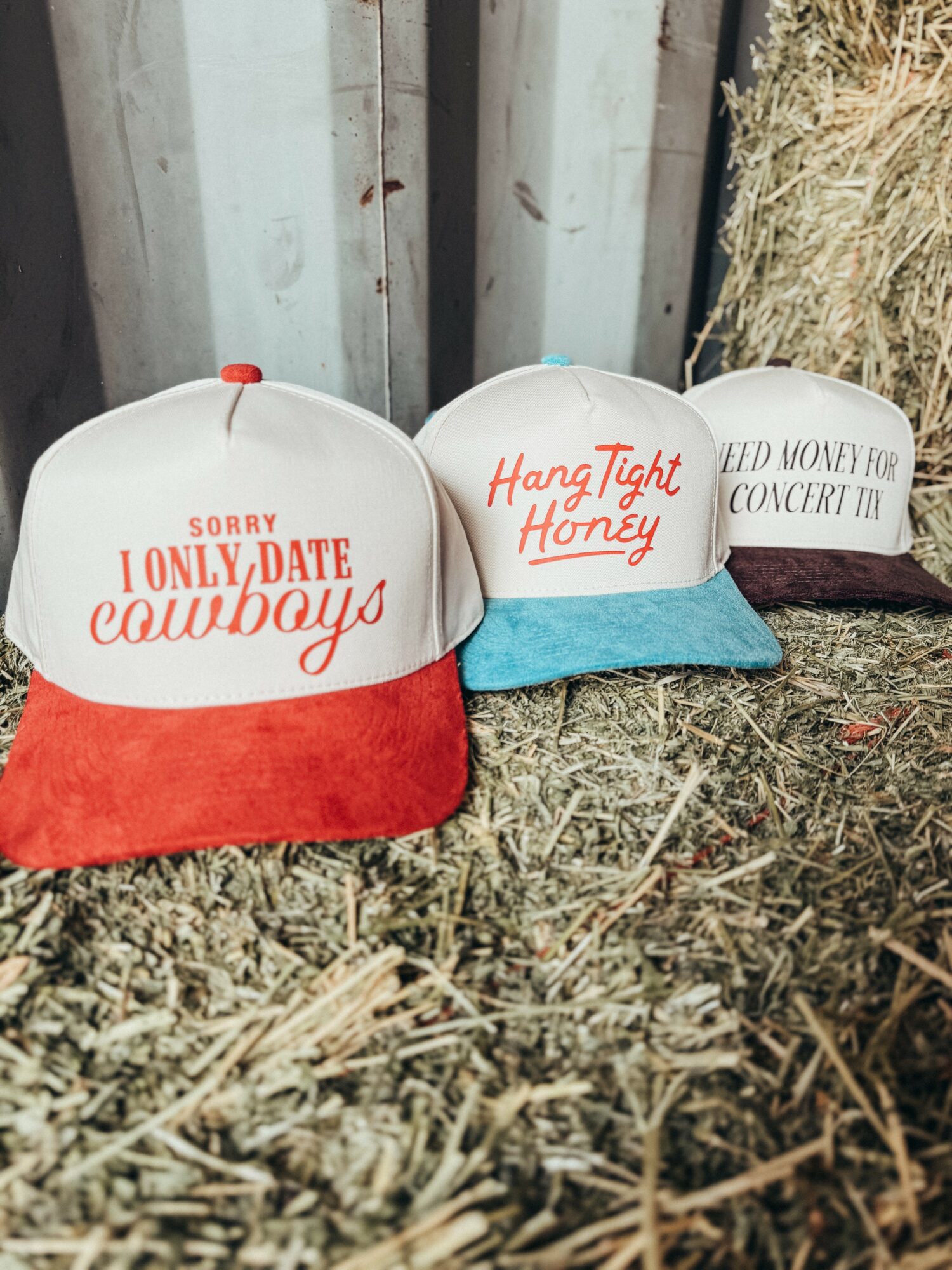 Two baseball caps on hay, one with red brim and white front reading 
