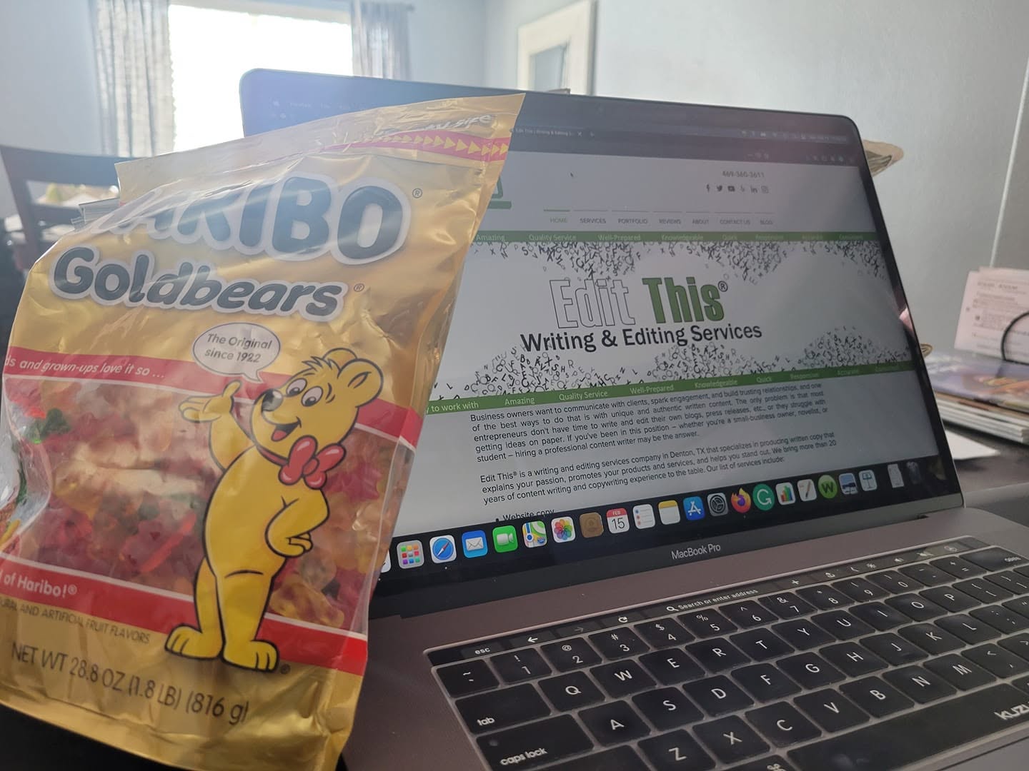 Laptop on table with a website open, bag of Goldbears gummy candies in front, room with window in background.